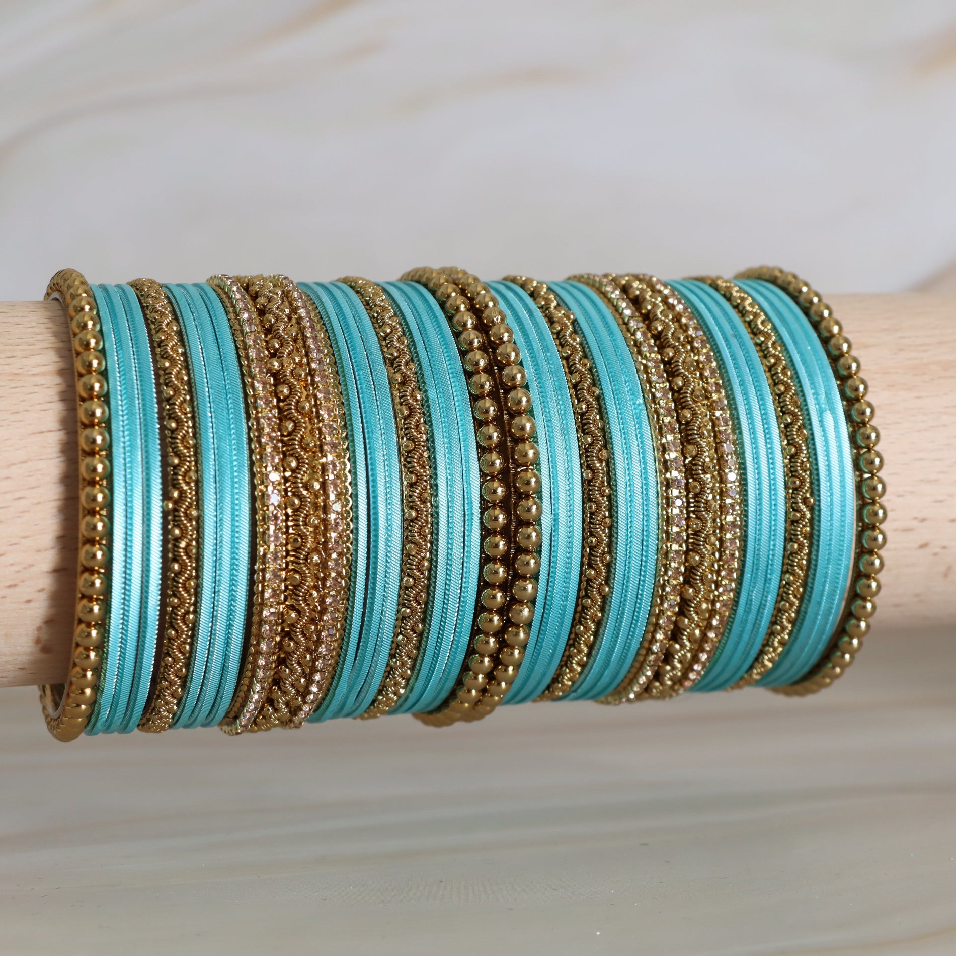 Turquoise and gold bangles stacked on a wooden stick against a light background