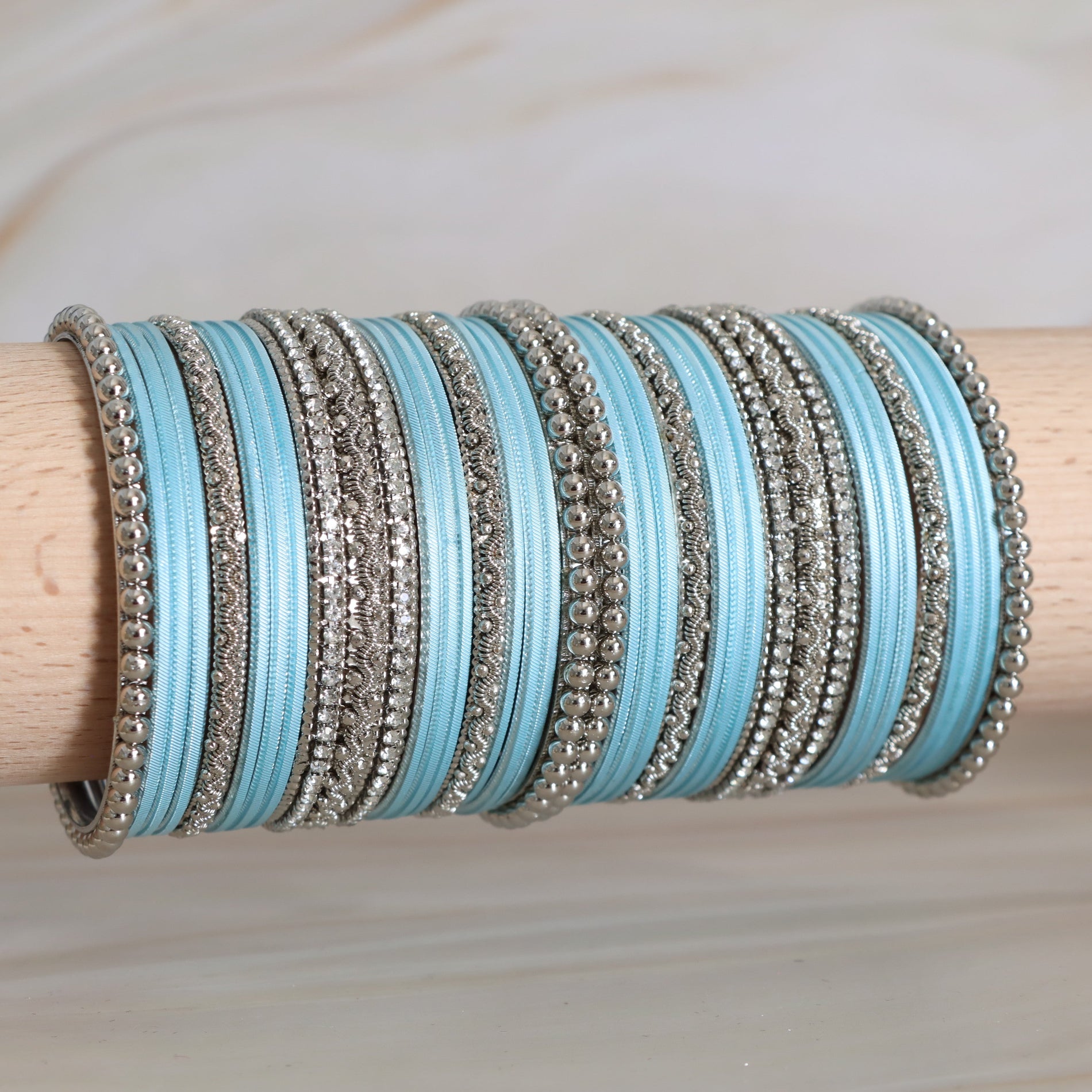 Stack of blue and silver bangles on a wooden stick against a neutral background