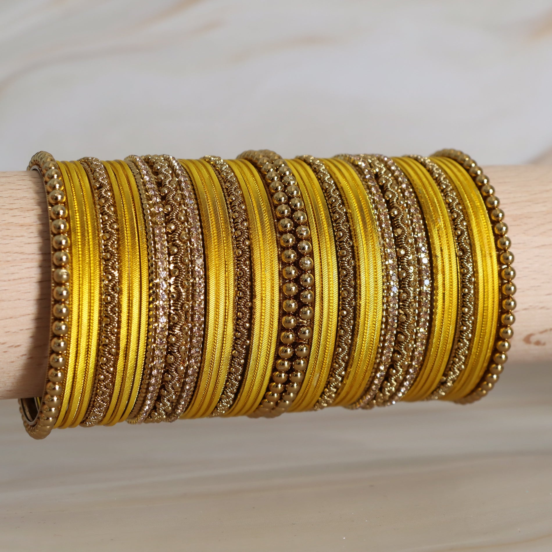 Stack of gold and yellow bangles on a wooden stick against a neutral background