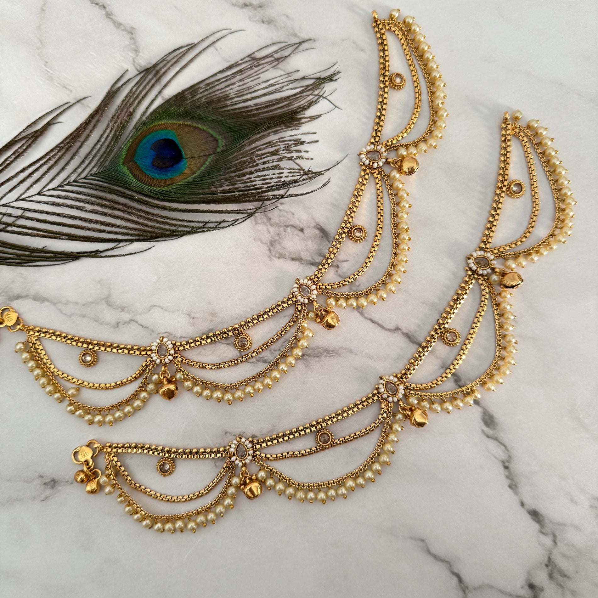 Gold anklet with peacock feather on marble background