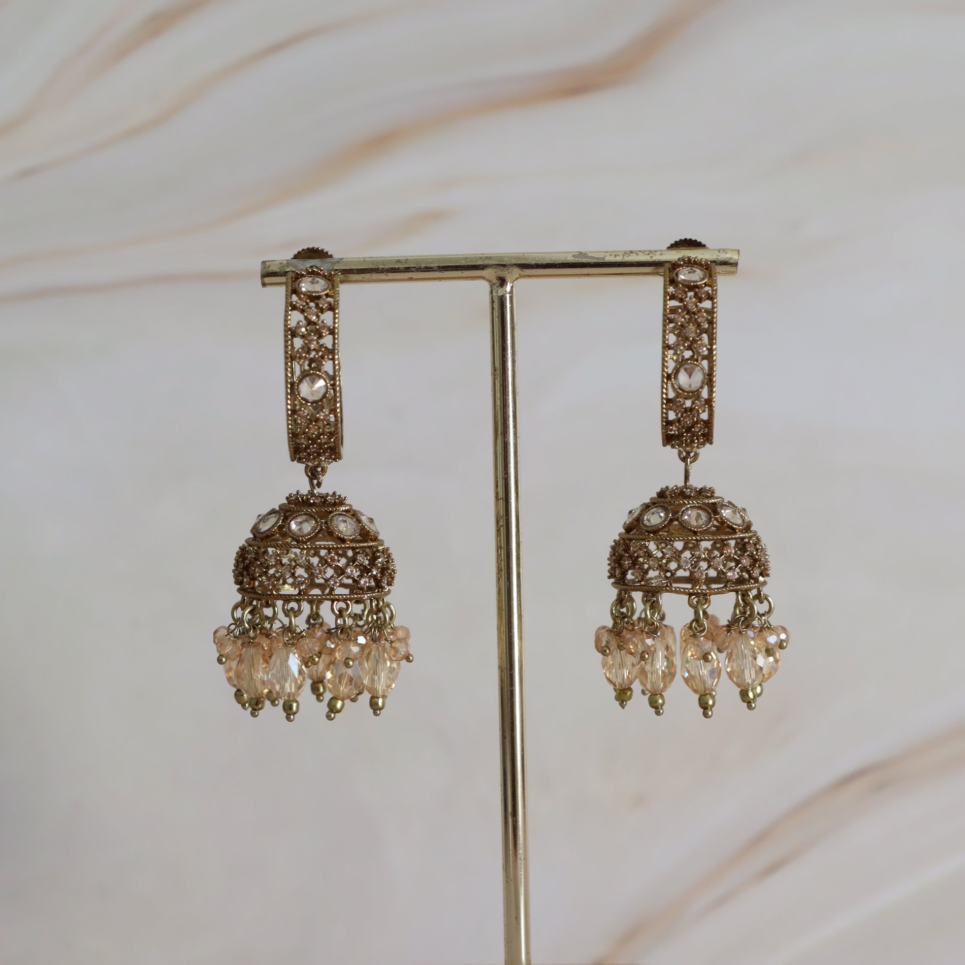 Ornate earrings on a stand against a neutral background