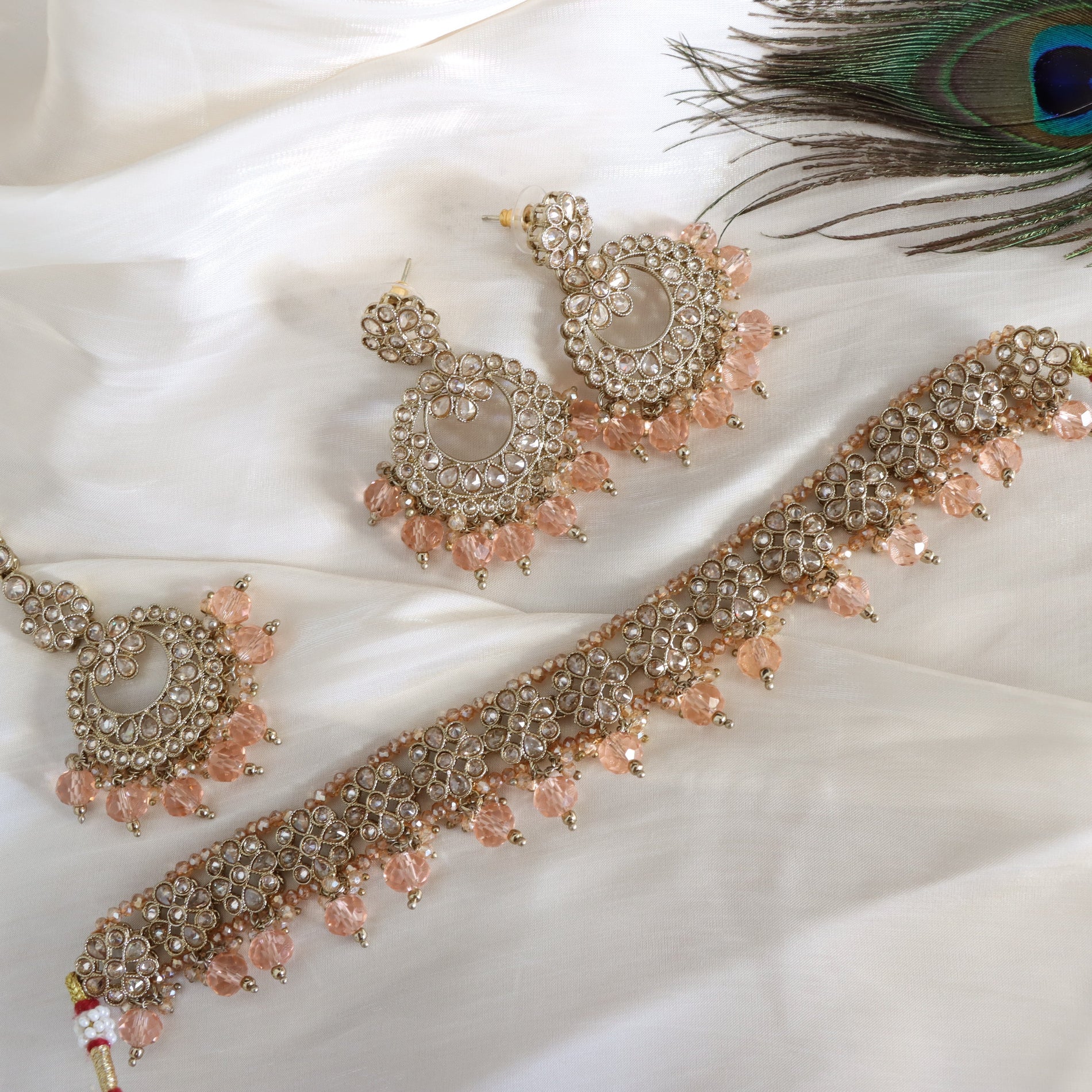 Ornate jewelry set with pink beads on a white fabric background