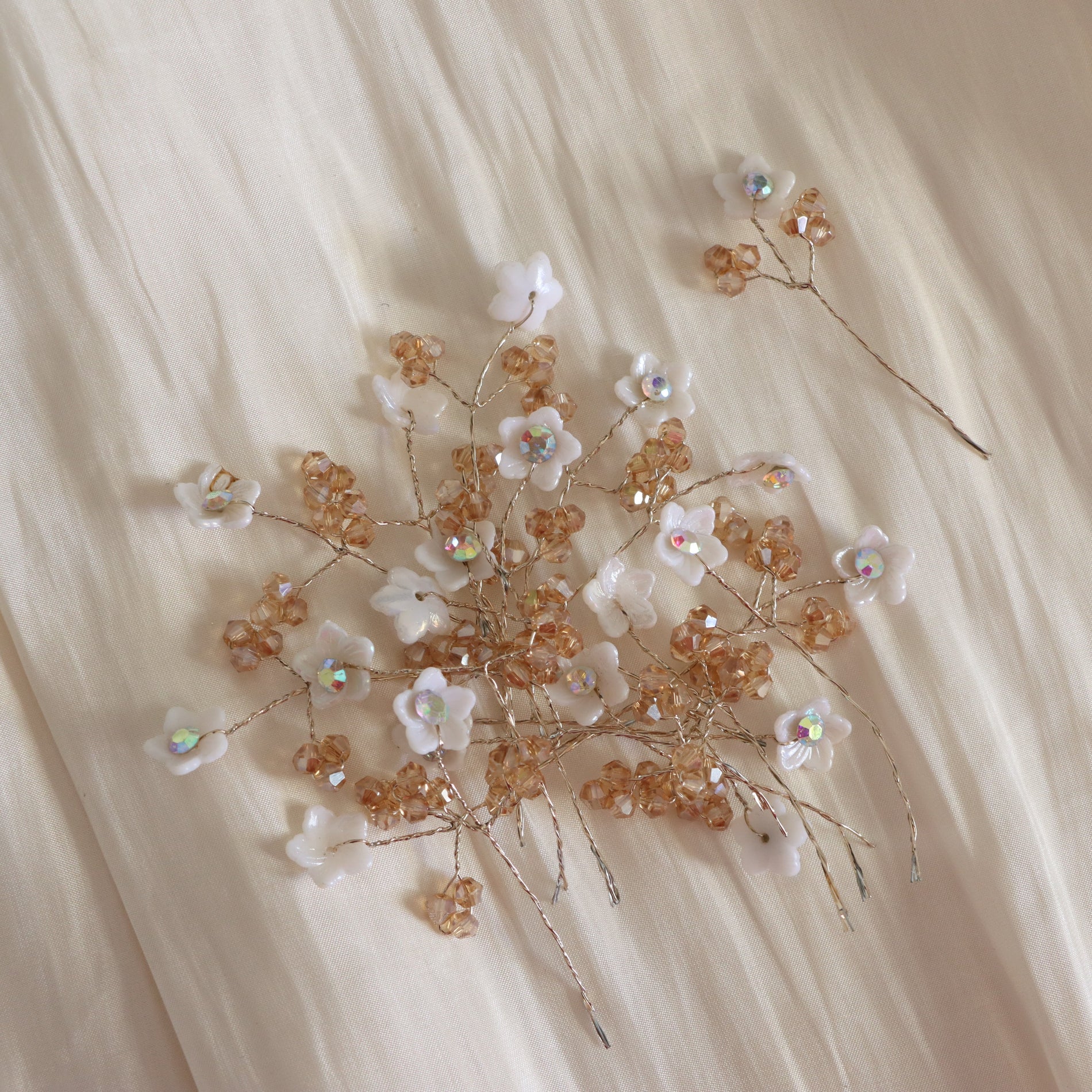 A delicate floral hair accessory set featuring small white flowers and tan/golden beads on thin wire stems, arranged on a soft cream fabric background.