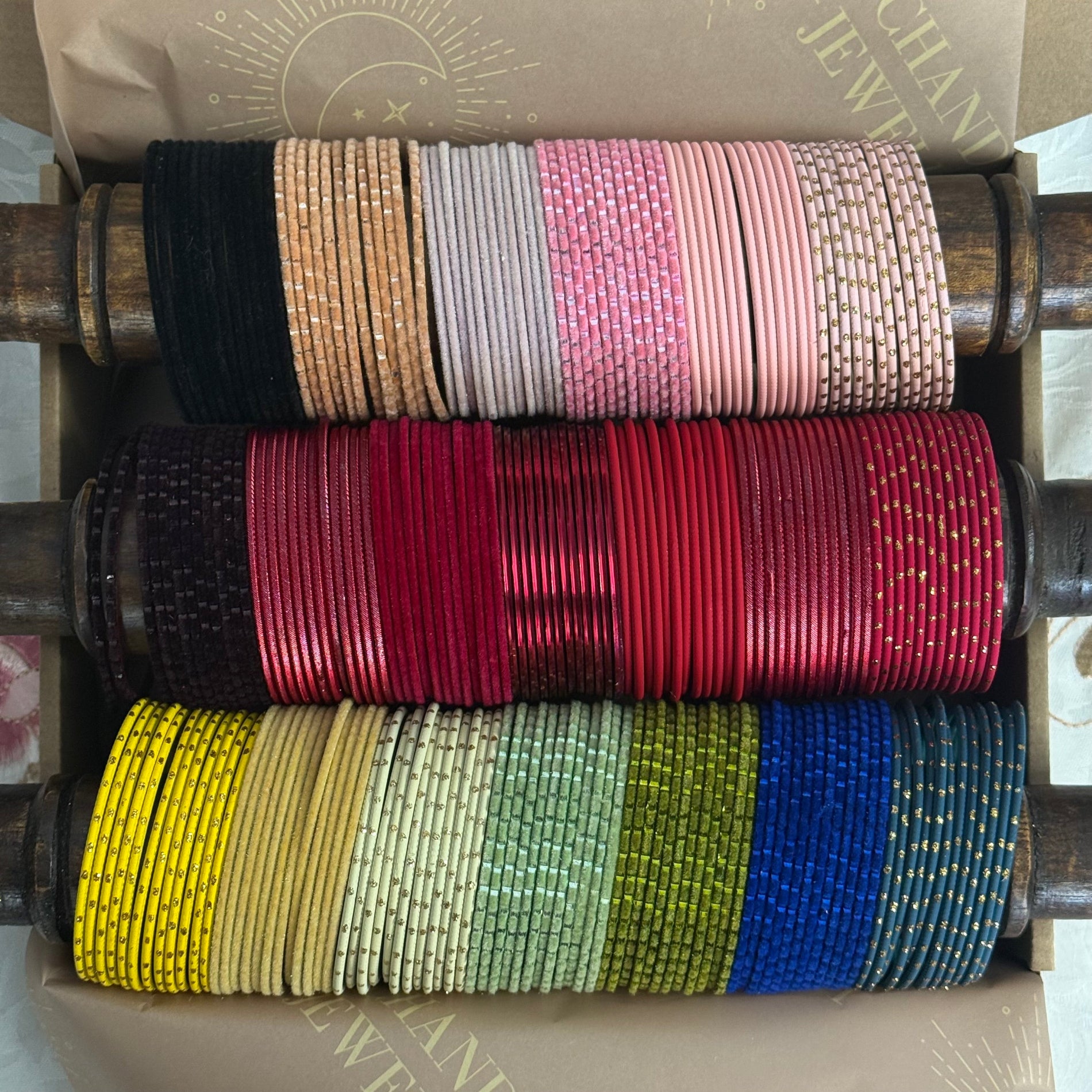 Stack of colorful bangles on a wooden roller, with a branded box in the background.