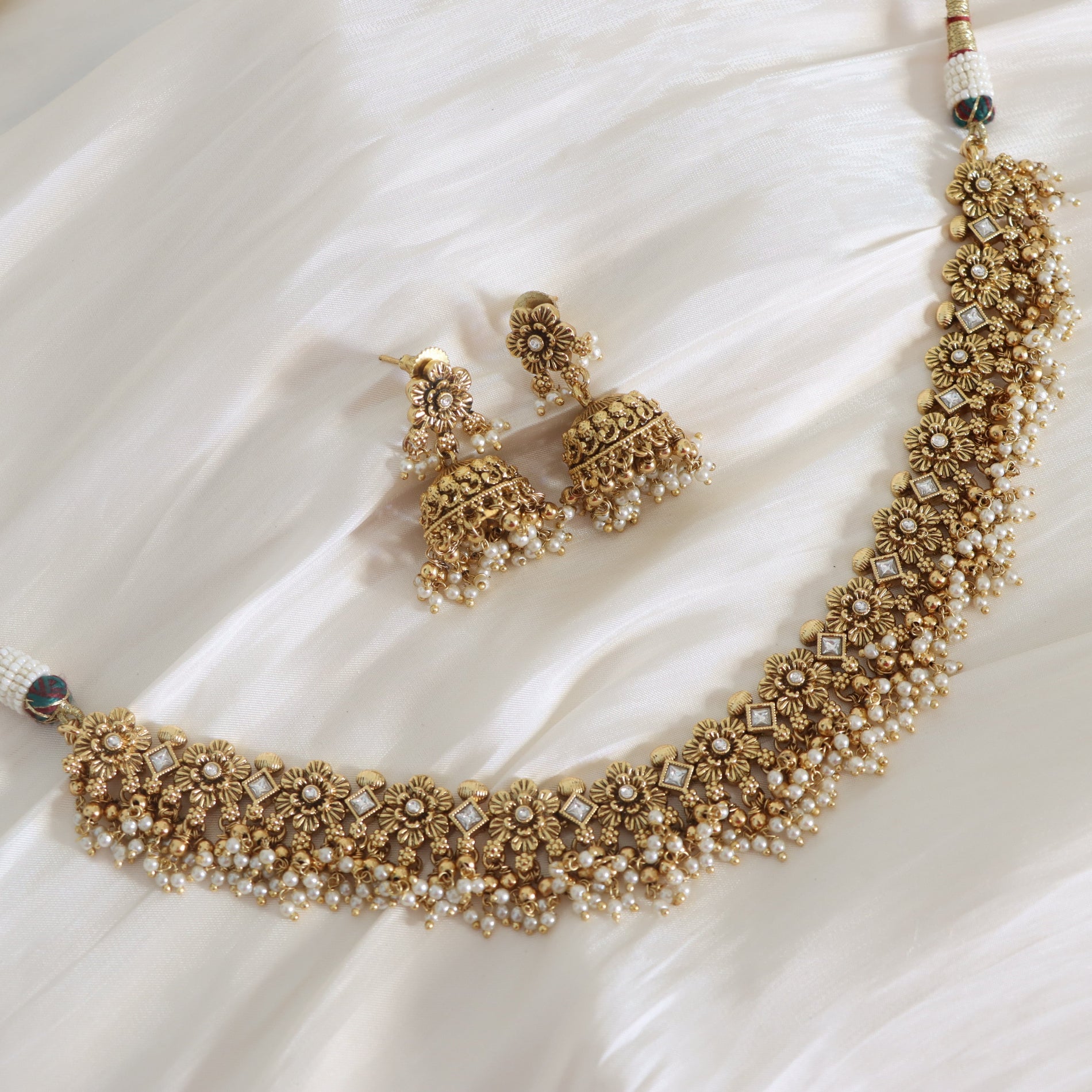 Ornate gold necklace and earrings on a white fabric background