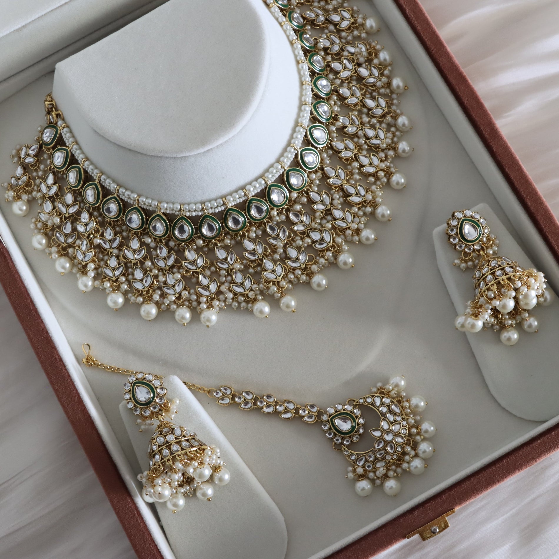 Gold and white pearl jewelry set displayed in an open presentation box, including a statement necklace, matching earrings, and a necklace with a chain.