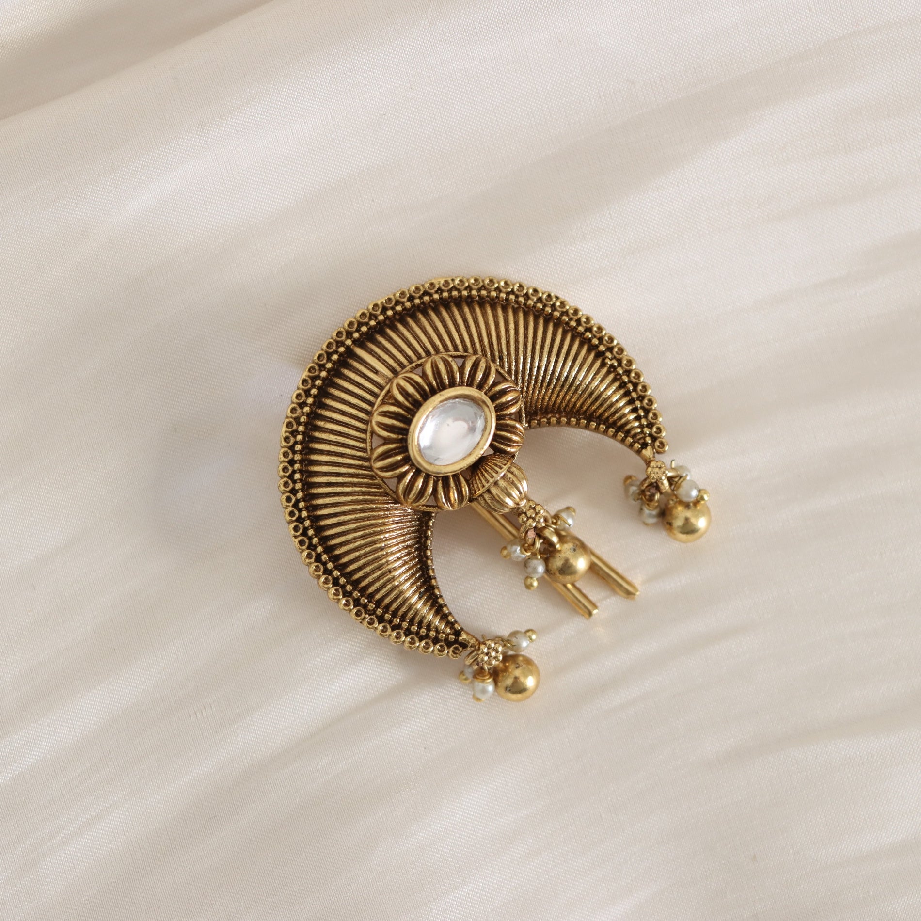 Gold brooch with intricate design on a beige fabric background