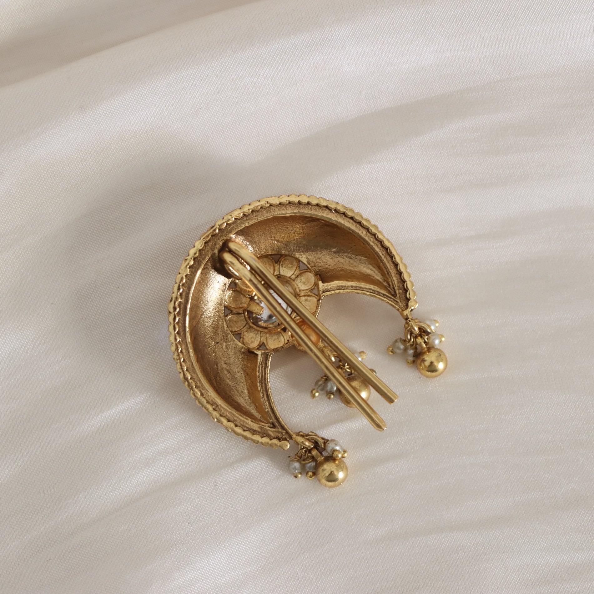 Gold brooch with intricate design on a white fabric background