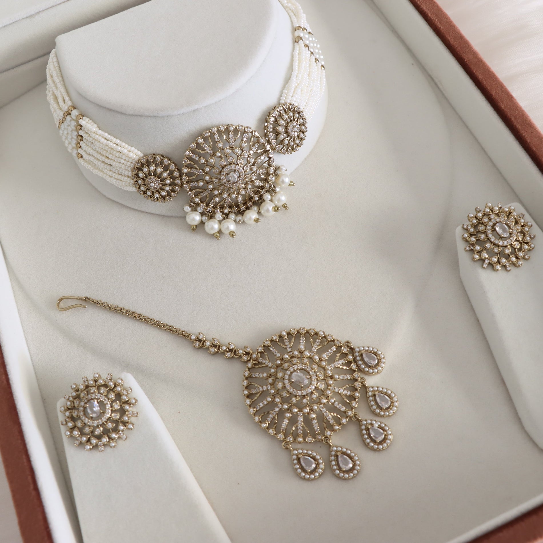 Jewelry set including a necklace, earrings, and bangles on a white cushioned surface.