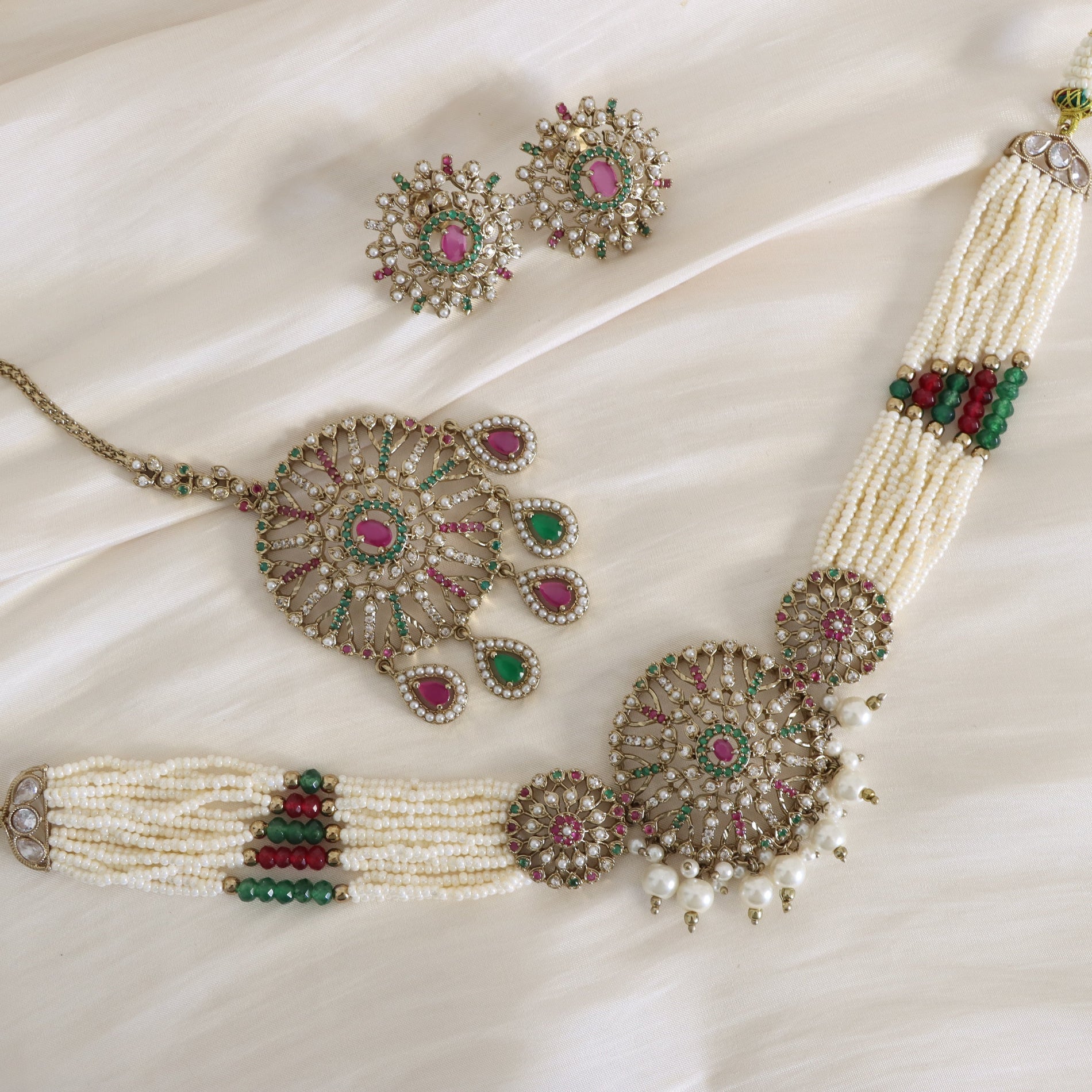 Ornate jewelry set with pearls, gemstones, and tassels on a satin surface