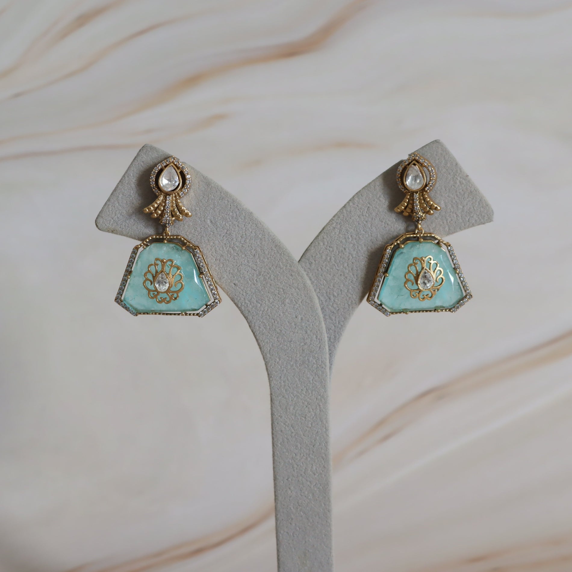 Pair of turquoise earrings on a gray stand with a marble background