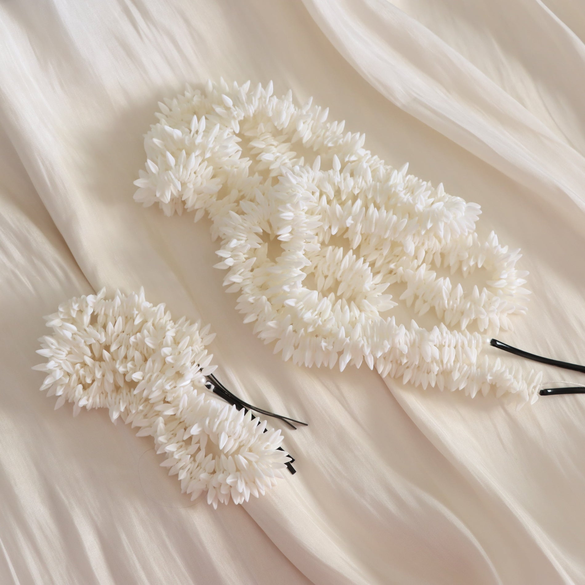Two white textured hair claw clips with black elastic bands, arranged on a draped cream-colored fabric background.
