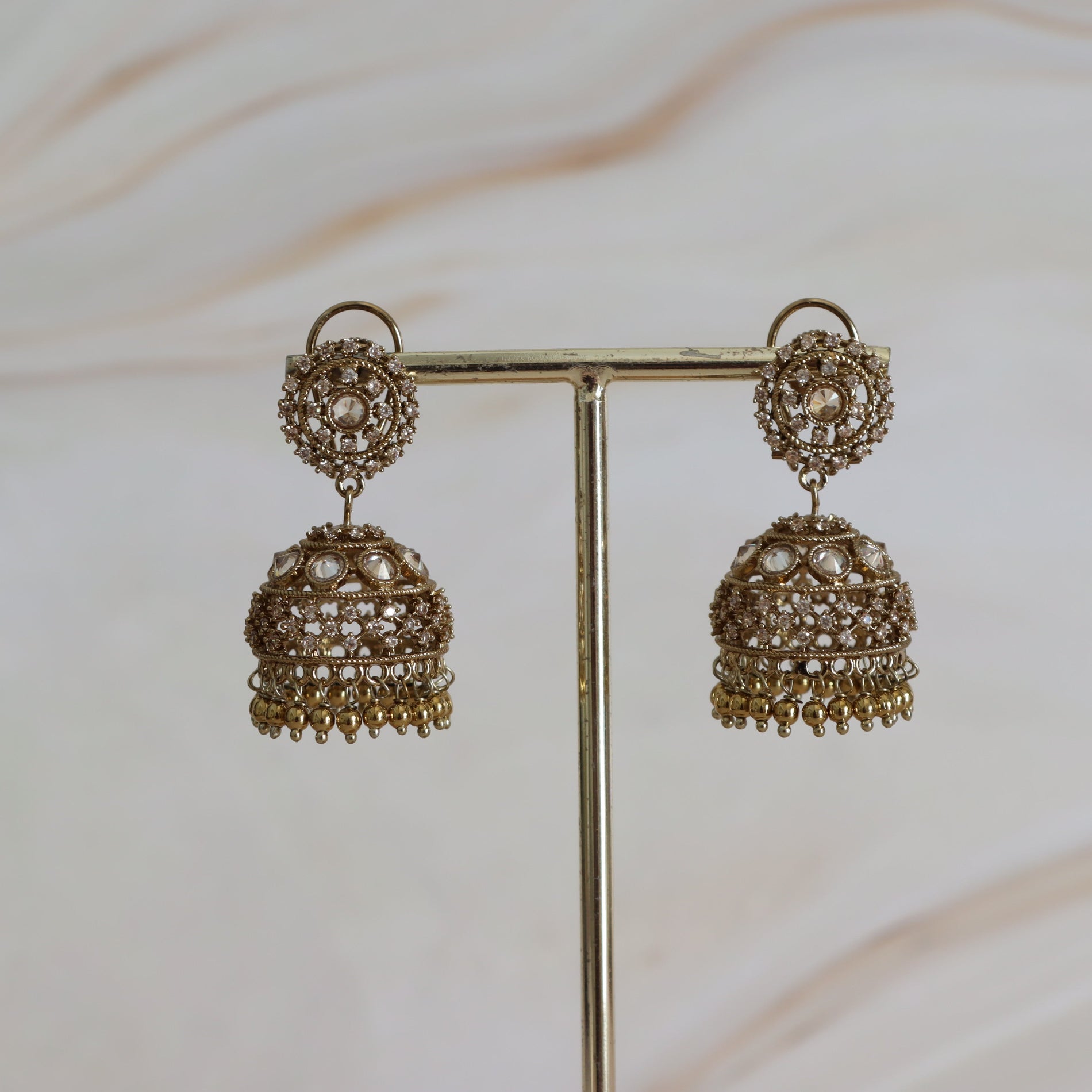 Pair of ornate gold earrings on a stand against a neutral background