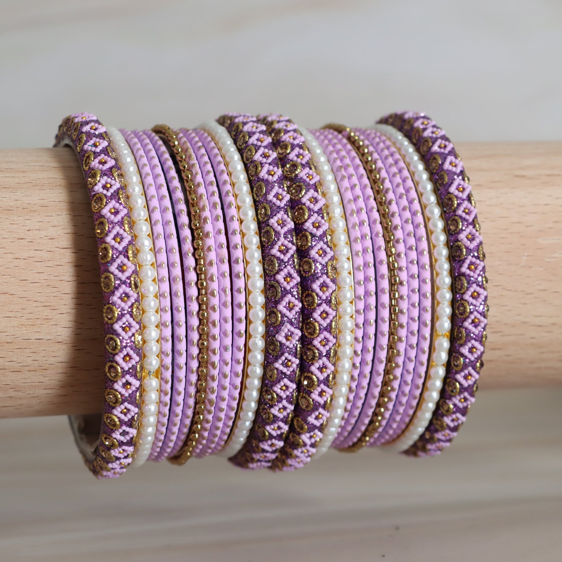 Set of purple, gold, and white beaded bracelets on a wooden stick.