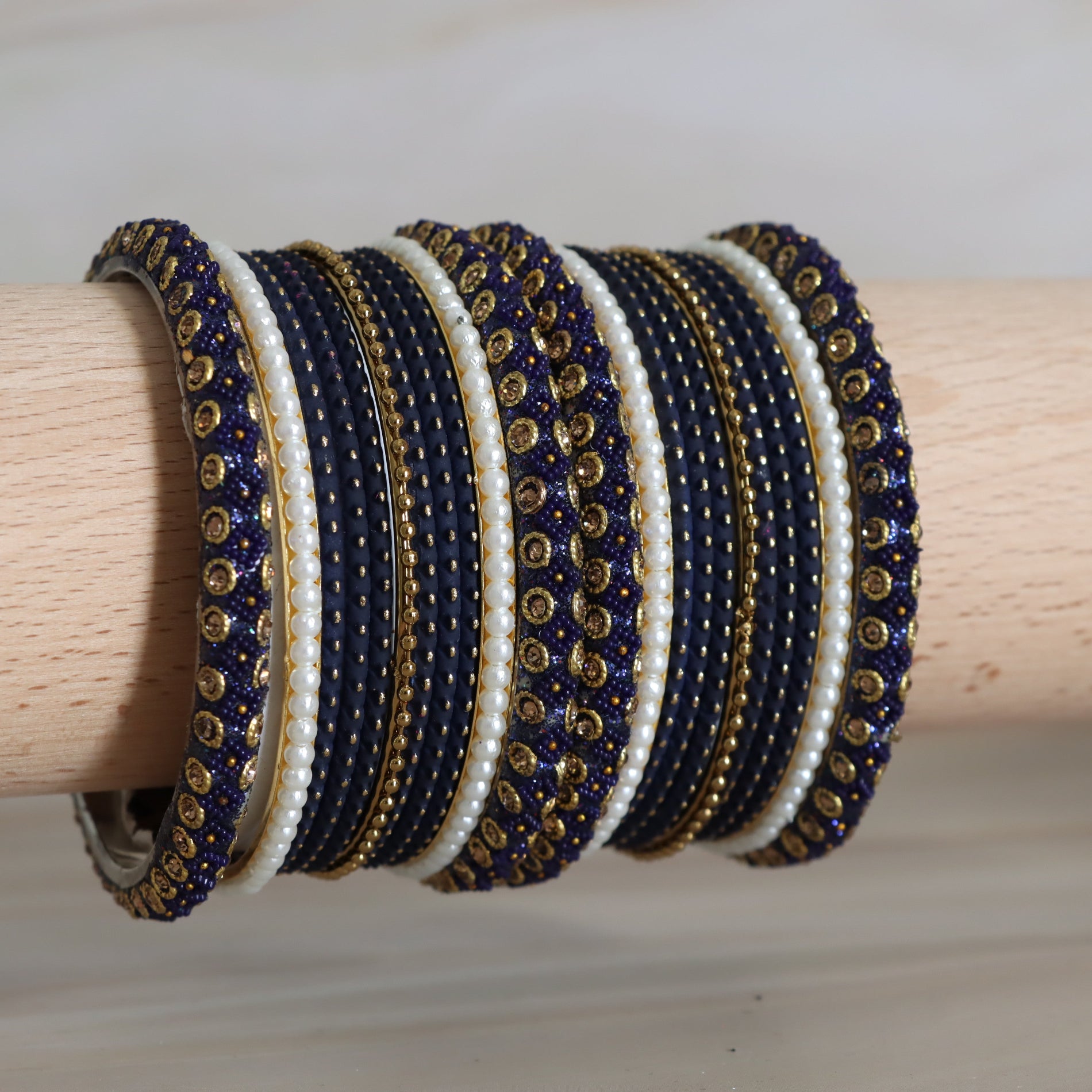 Set of blue, gold, and white beaded bracelets on a wooden stick.