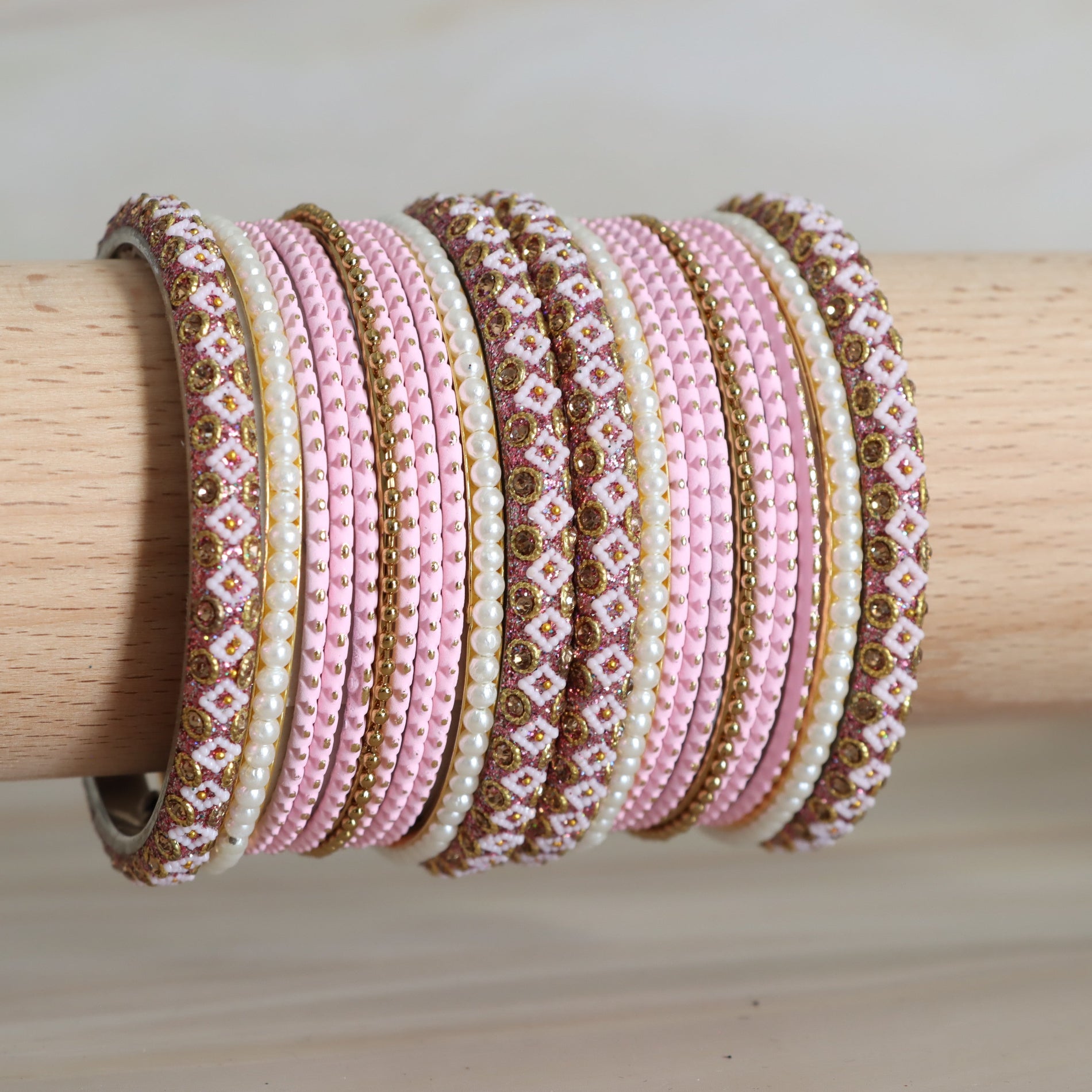 Set of pink, gold, and white beaded bracelets on a wooden stick.