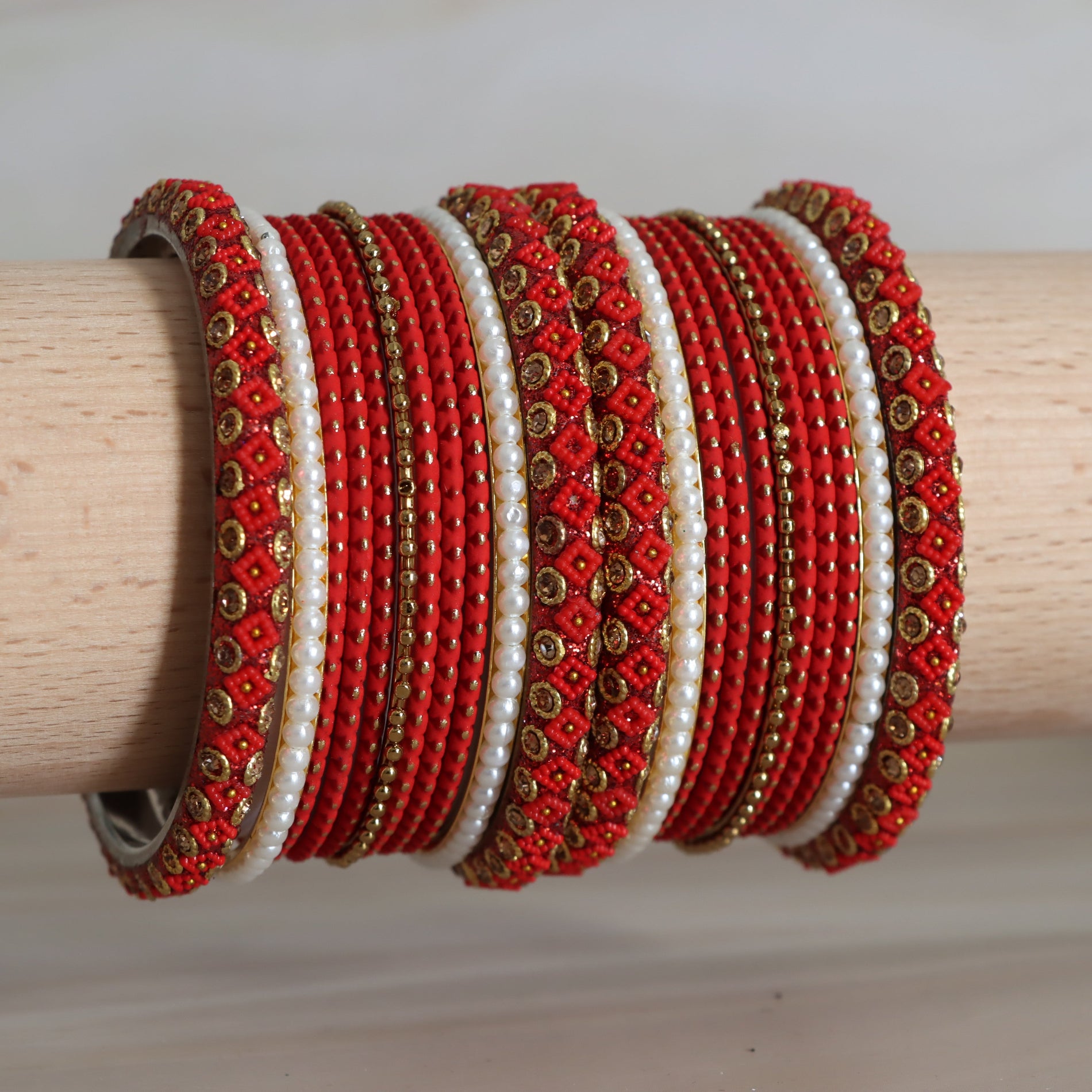 Set of red and white beaded bangles with gold accents on a wooden stick.