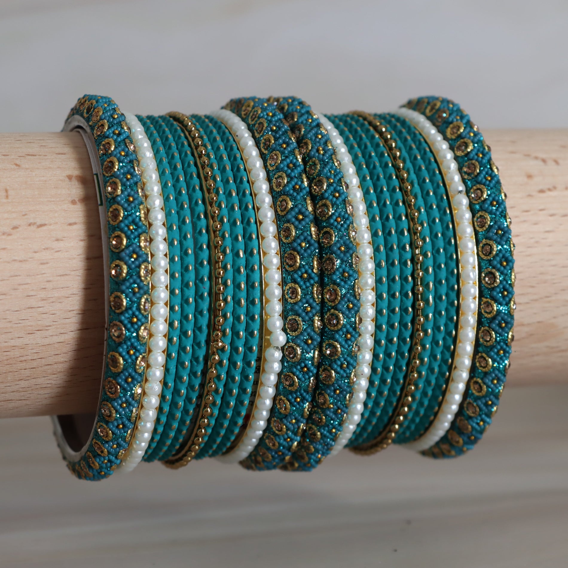 Set of turquoise and white beaded bangles with gold accents on a wooden stick.