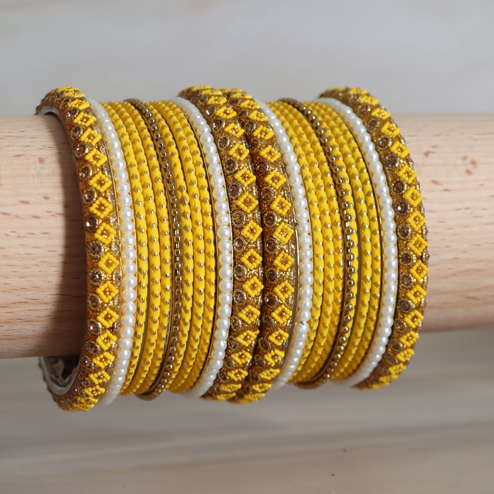 Yellow and white beaded bracelets on a wooden stick against a neutral background
