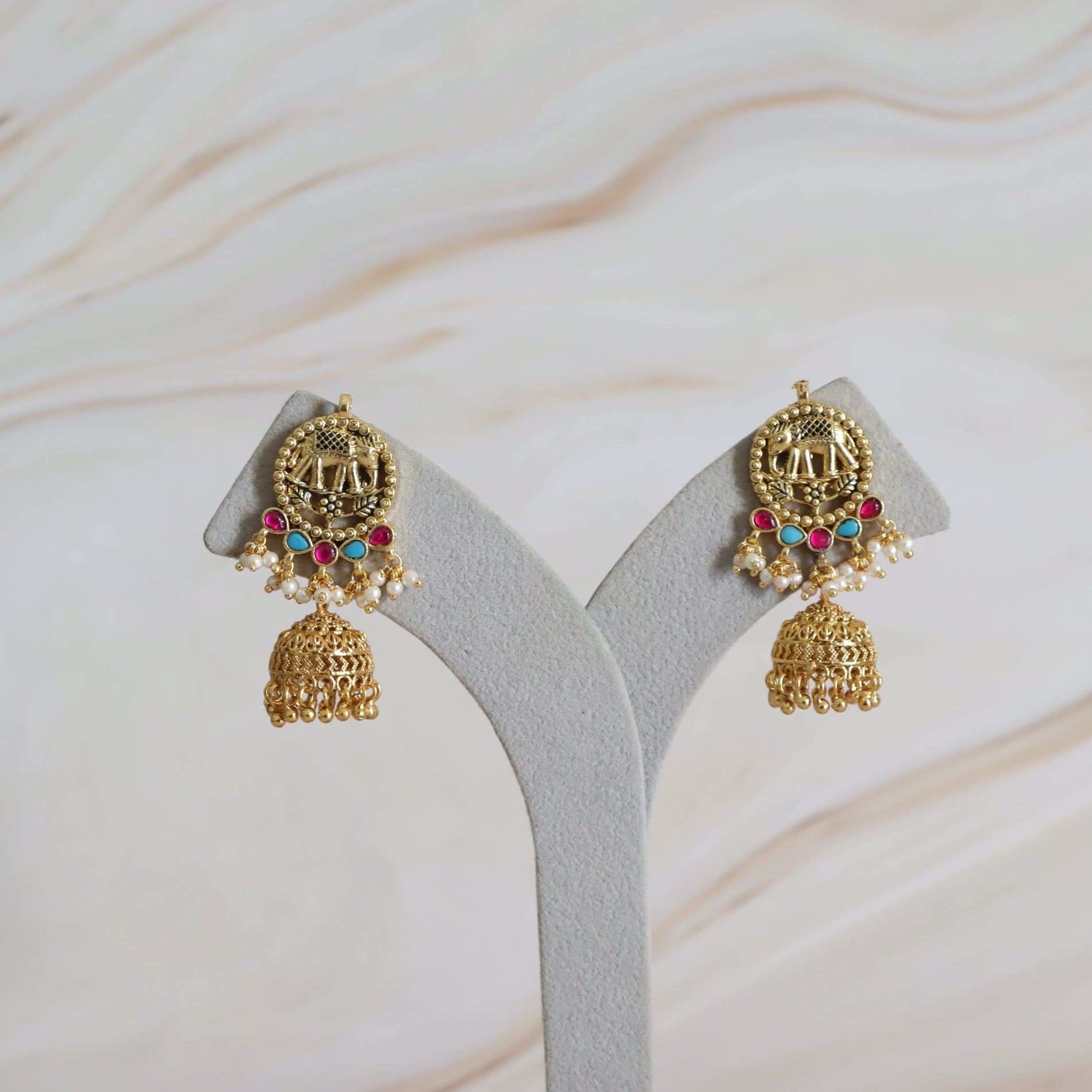 Pair of gold earrings with colorful gemstones on a gray stand against a light background
