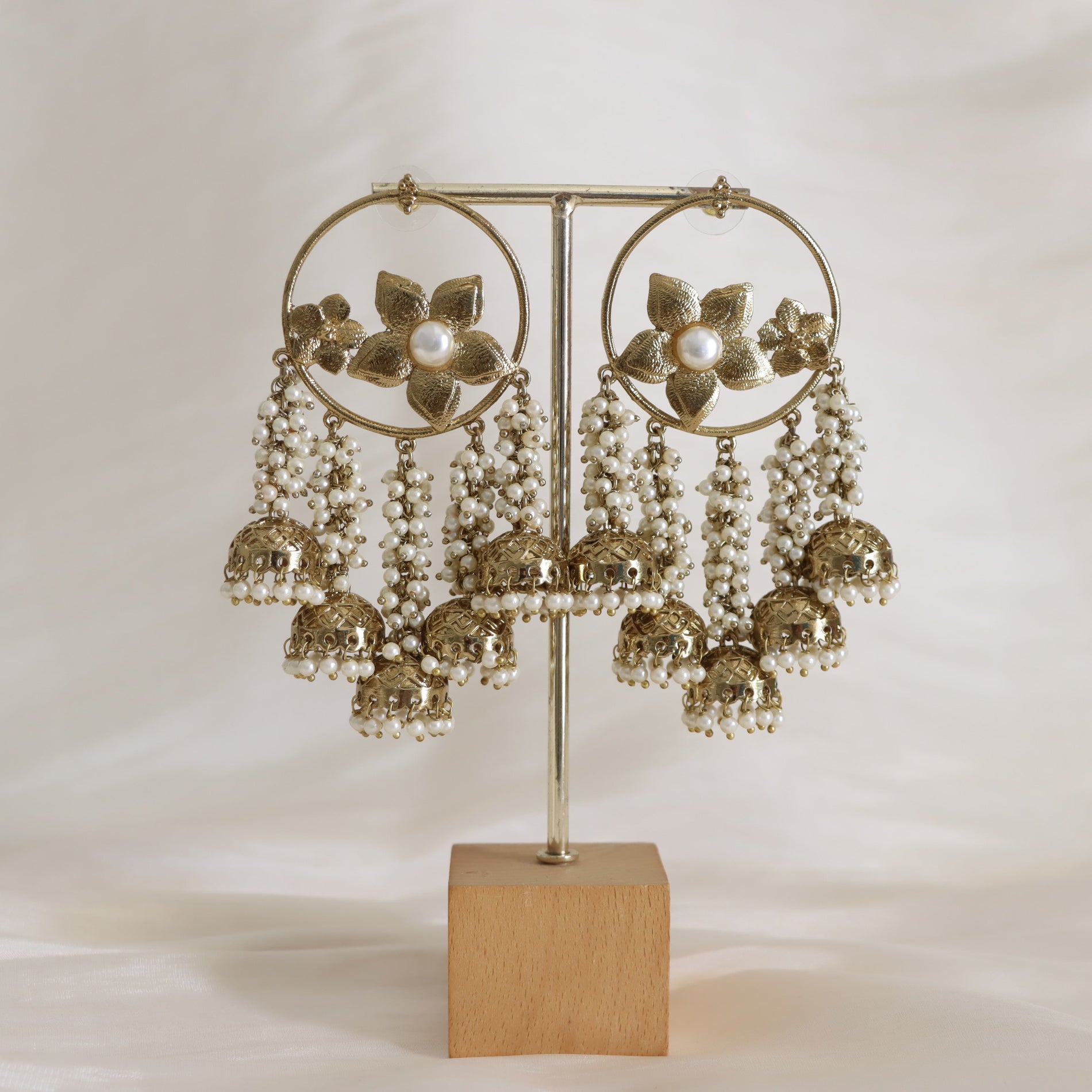 Decorative earrings with floral designs and pearl-like beads on a stand against a plain background