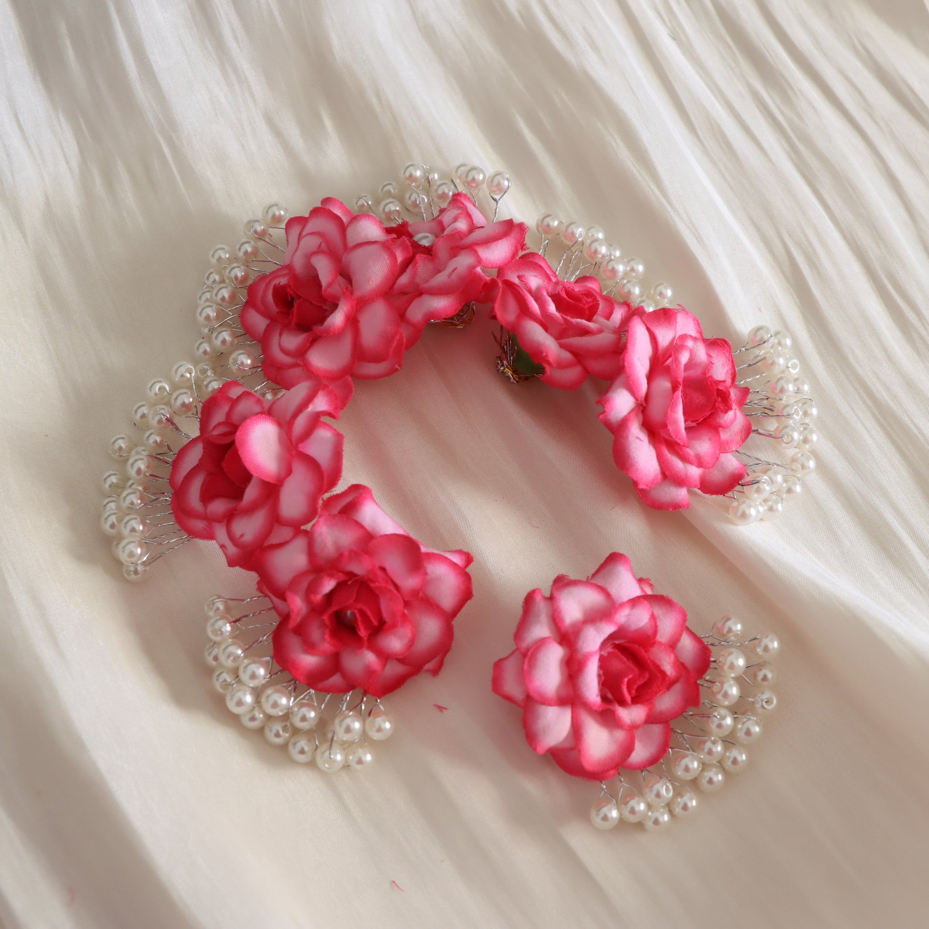 A set of pink and white artificial rose hair clips decorated with small white faux pearls, arranged on a draped cream fabric background.