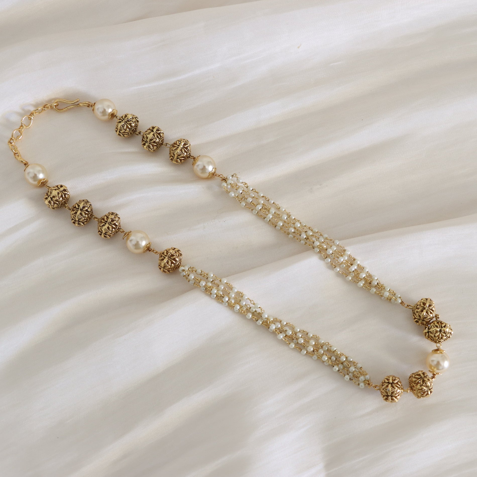 Gold and pearl beaded necklace on a textured white surface
