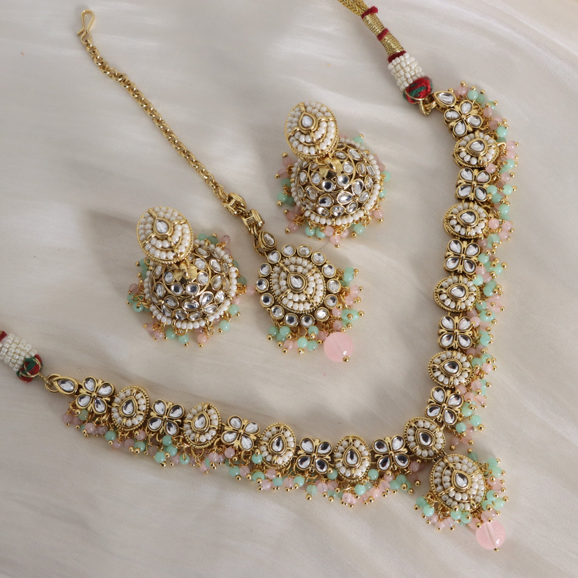 Ornate gold necklace with floral designs and pink beads on a white background