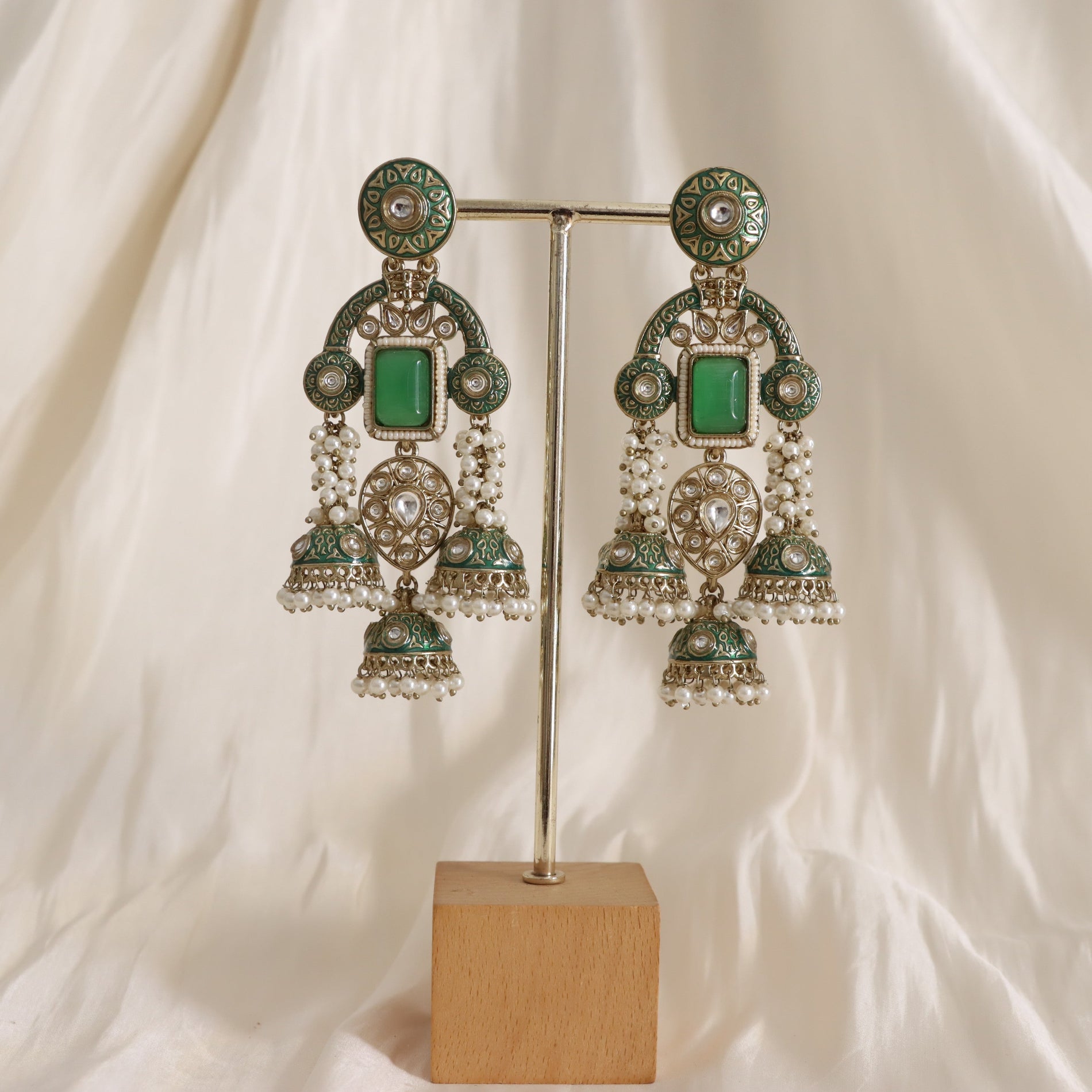 Ornate earrings with green gemstones on a stand against a white background