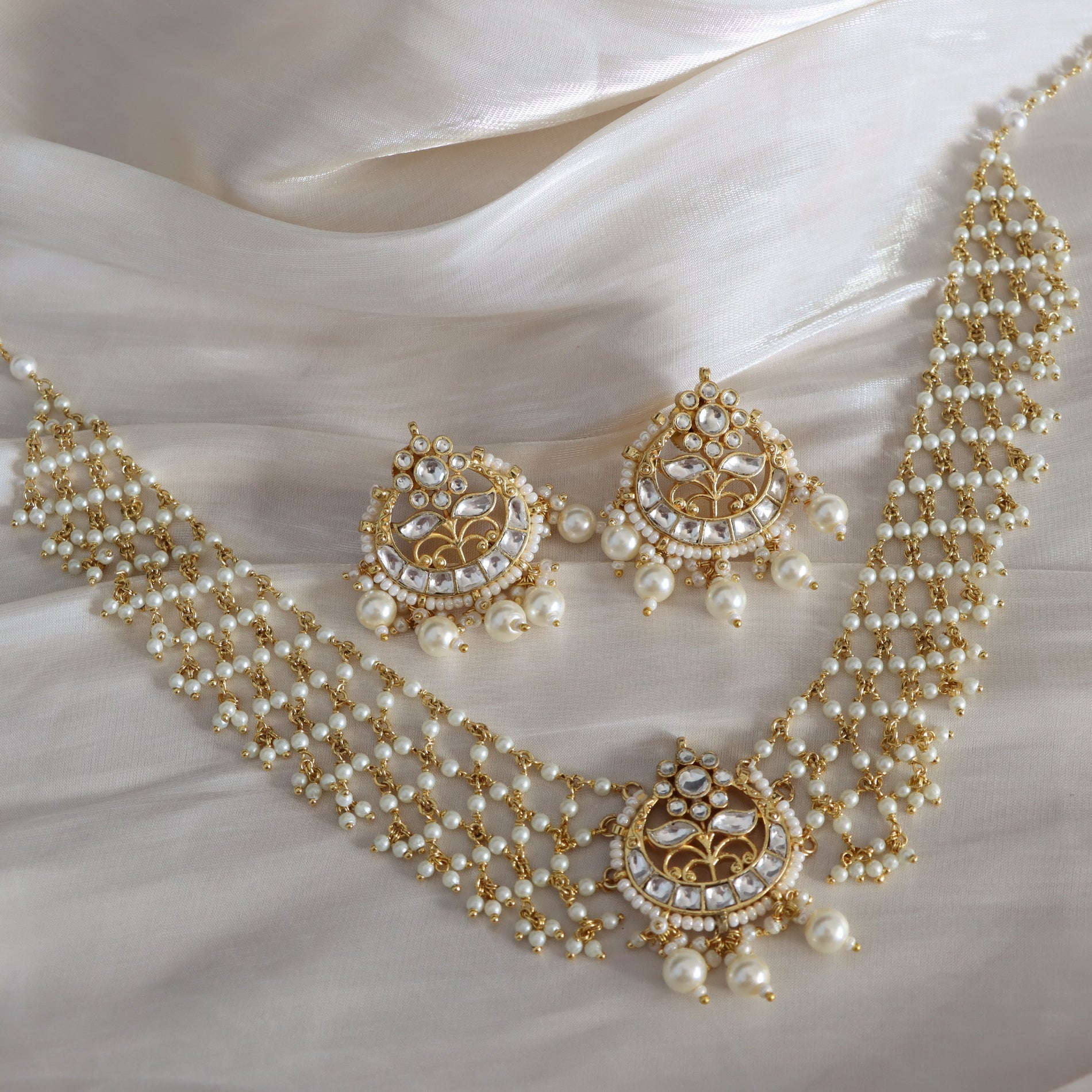 Pearl and gold jewelry set on a white fabric background