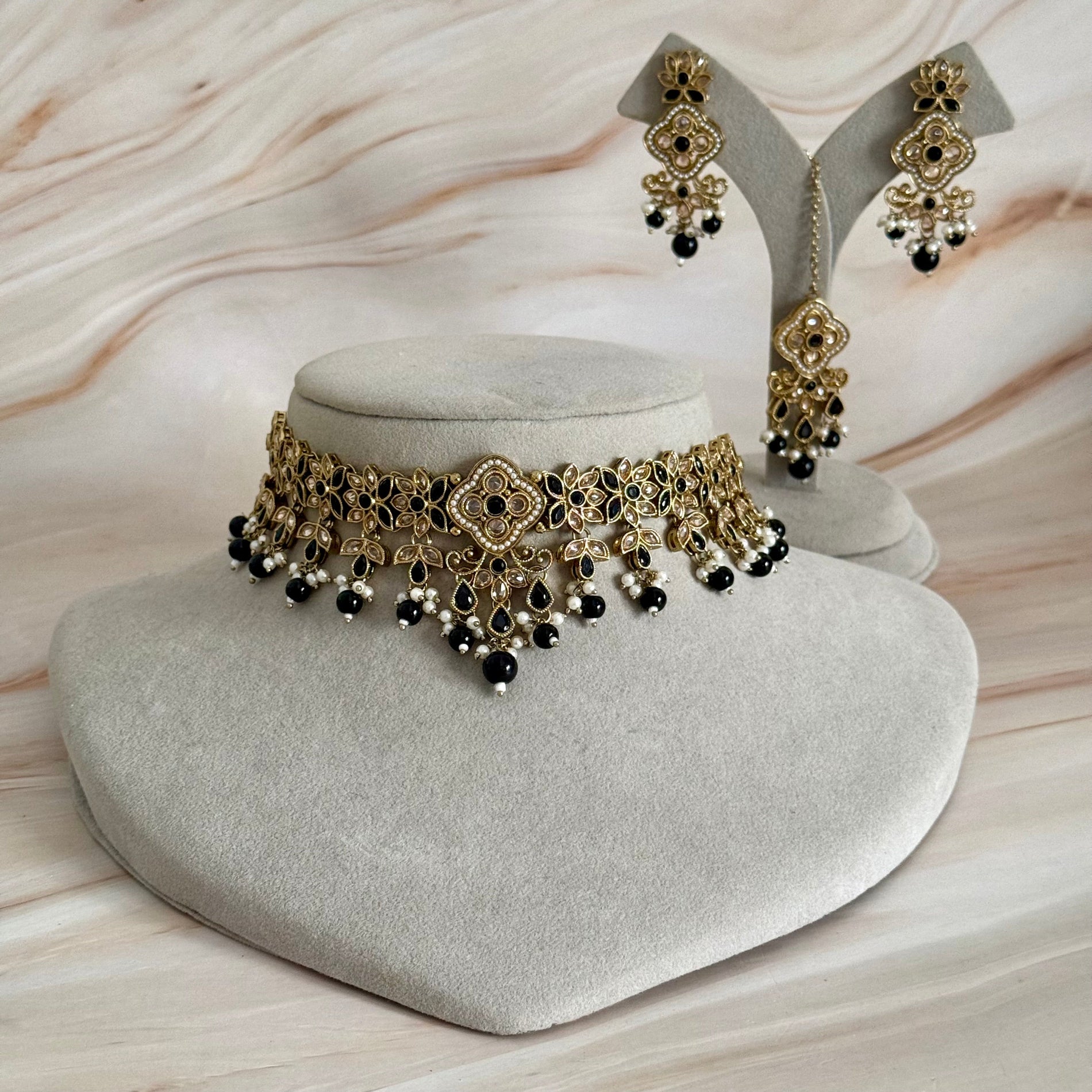 Gold and black jewelry set on a gray stand with a neutral background
