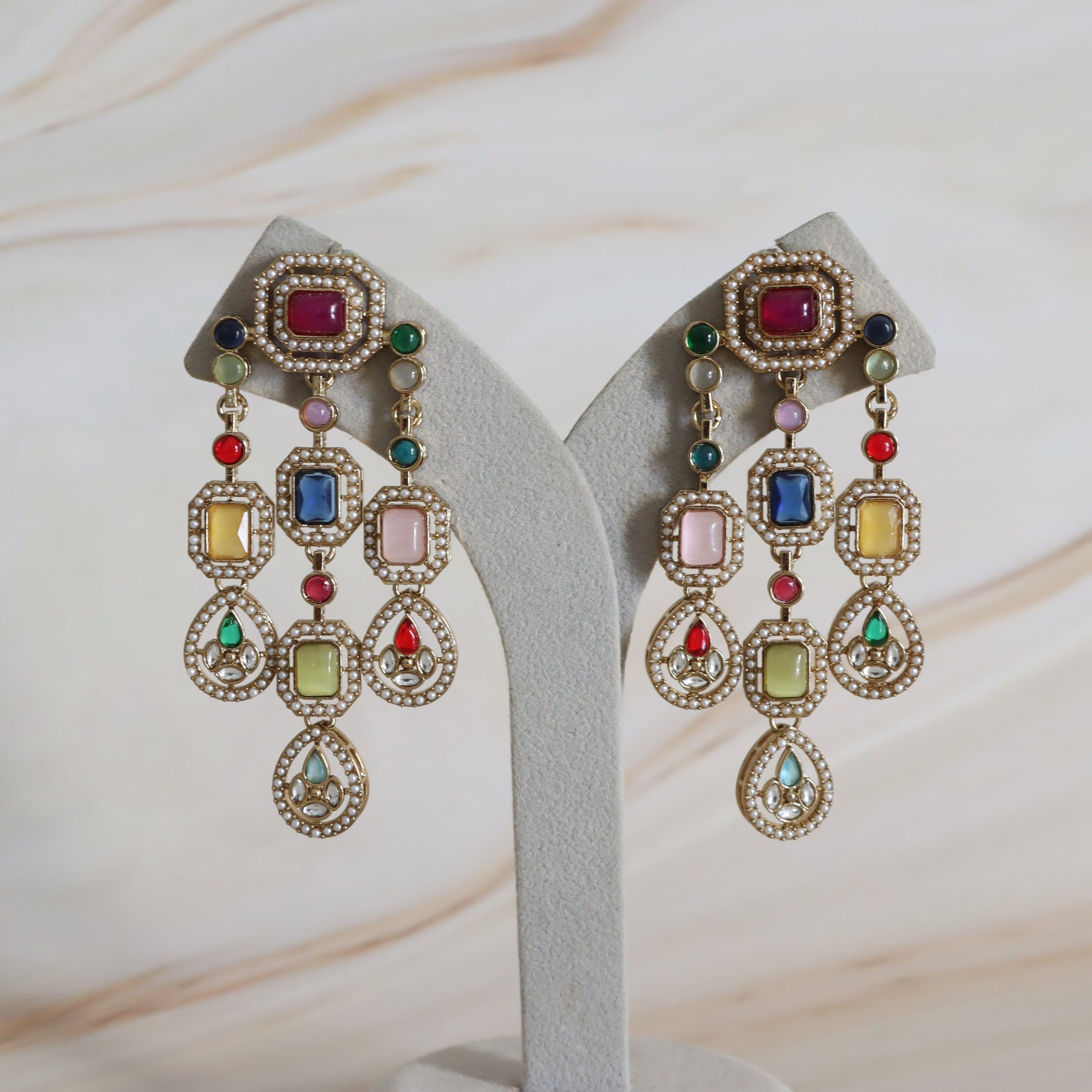 Colorful earrings with gemstones on a white stand against a light background