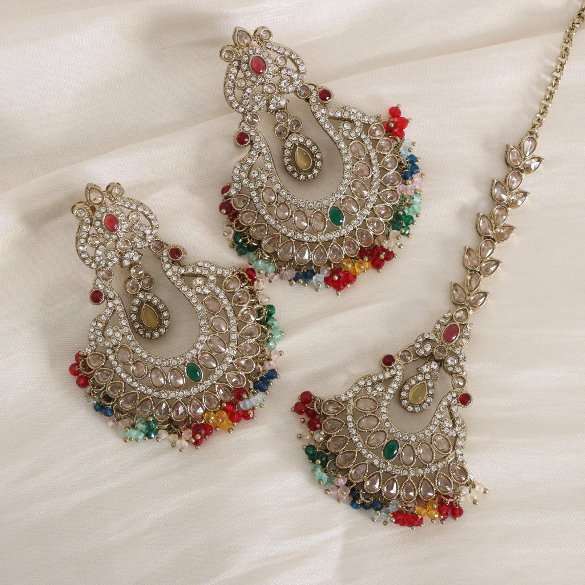 Ornate jewelry set with multicolored stones on a white fabric background