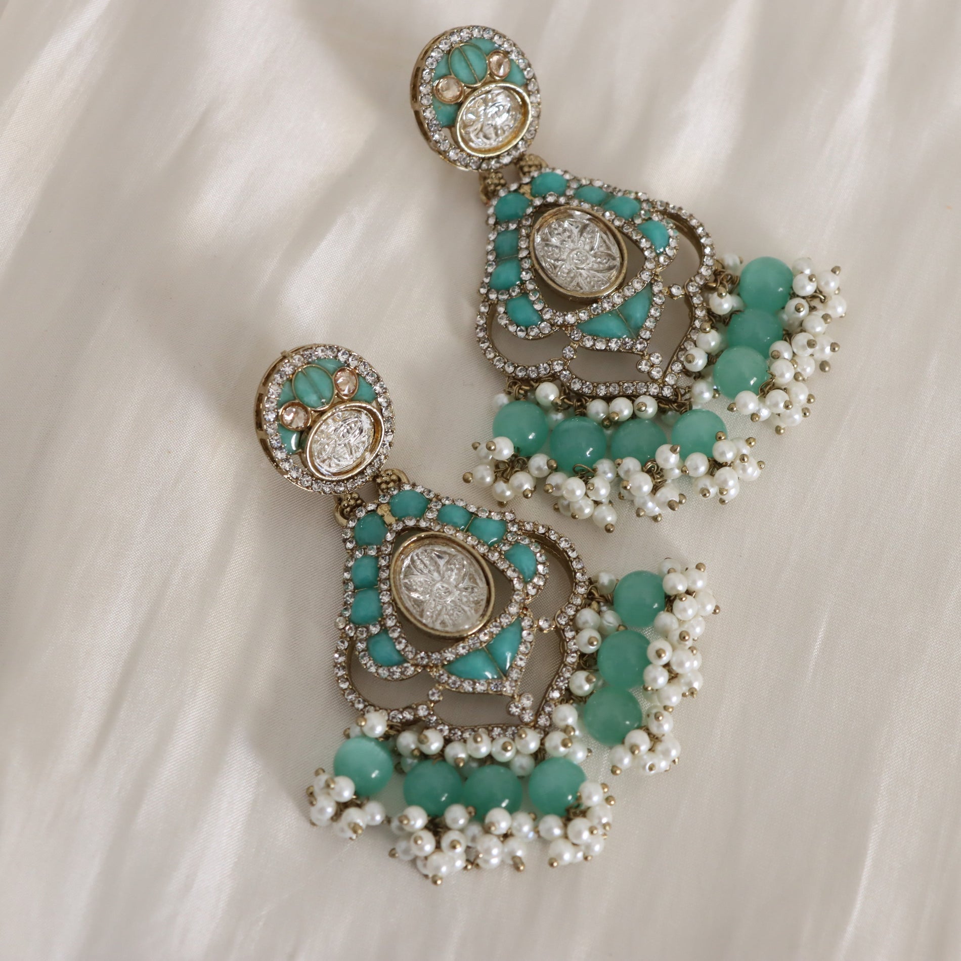 Pair of earrings with turquoise stones and pearl-like beads on a white fabric background