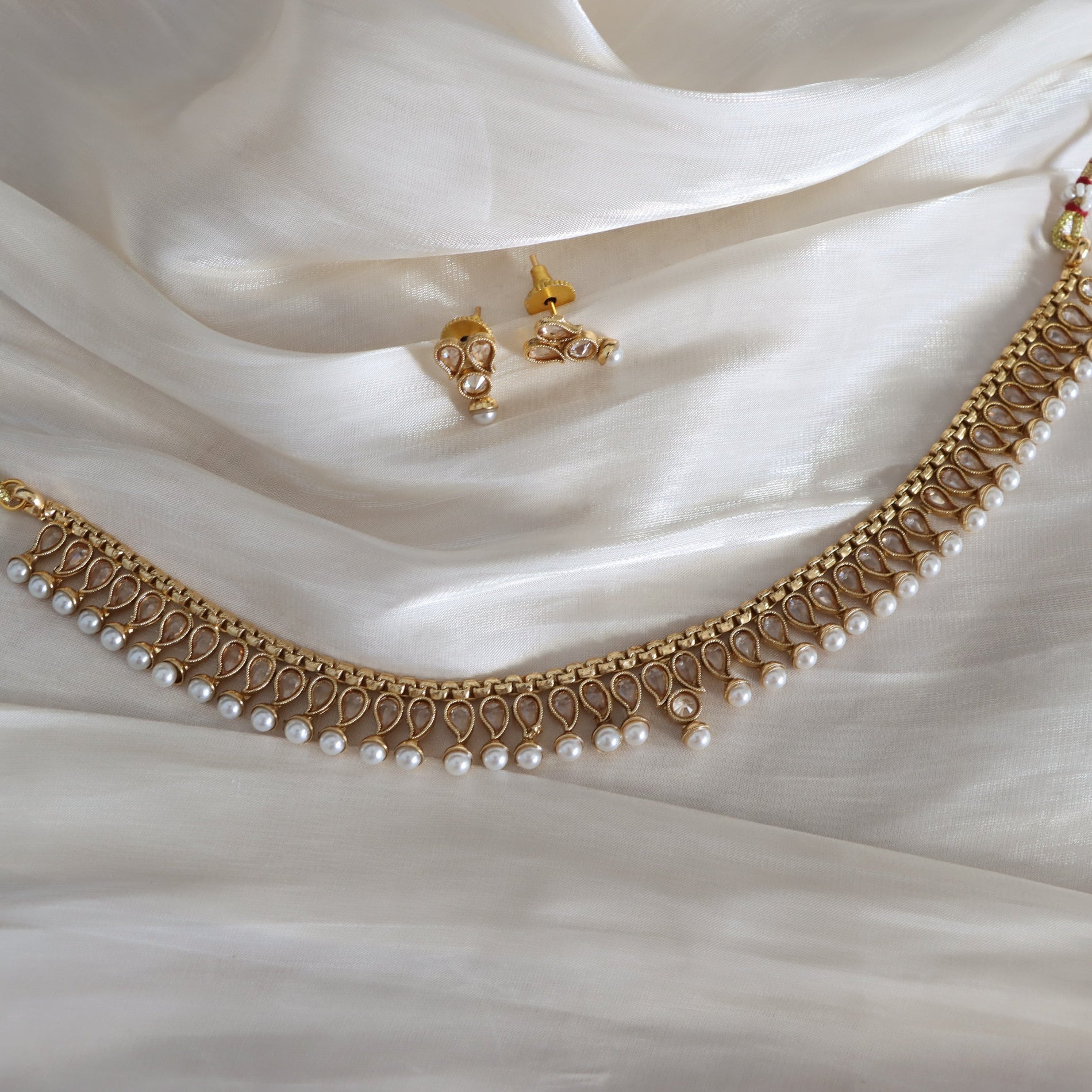Gold necklace with pearls and matching earrings on white fabric