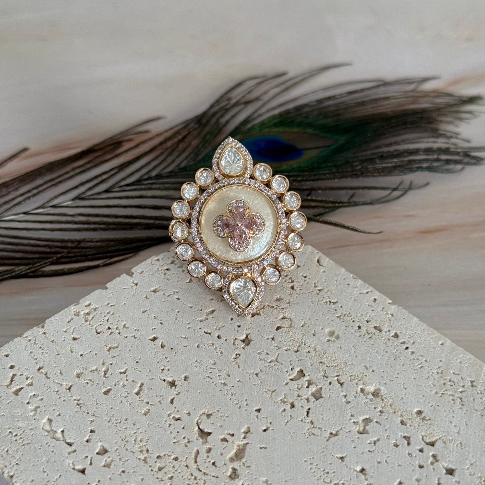 Decorative brooch with gemstones on a textured surface with a peacock feather in the background