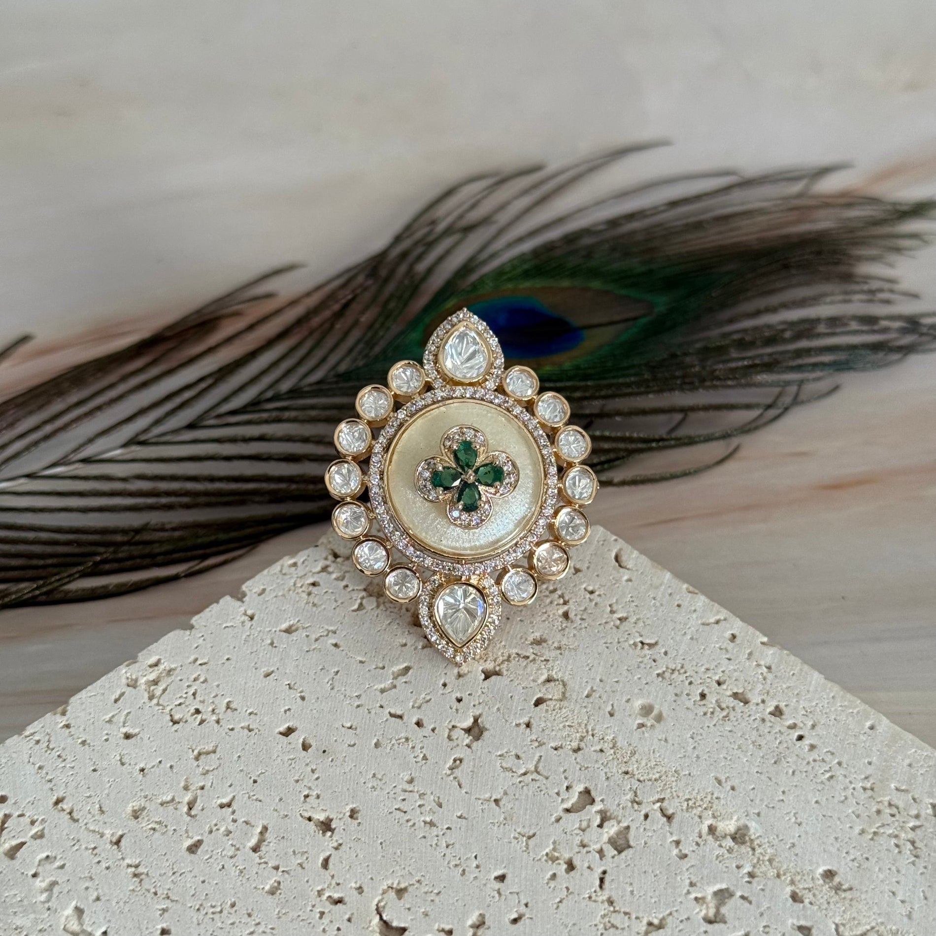 Decorative brooch with gemstones on a textured surface with peacock feathers in the background