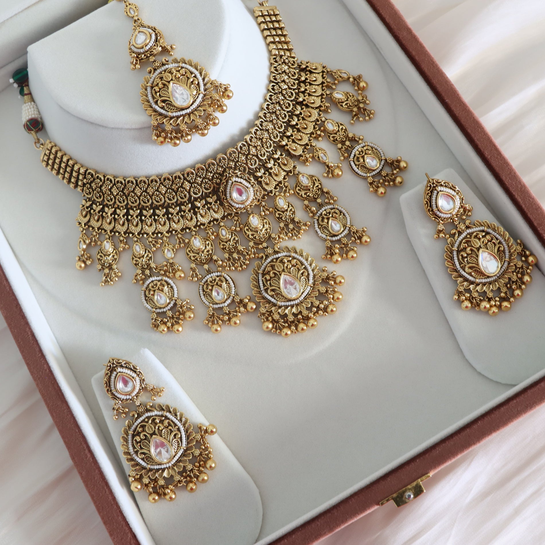 Gold jewelry set with necklace and earrings on a white cushioned box