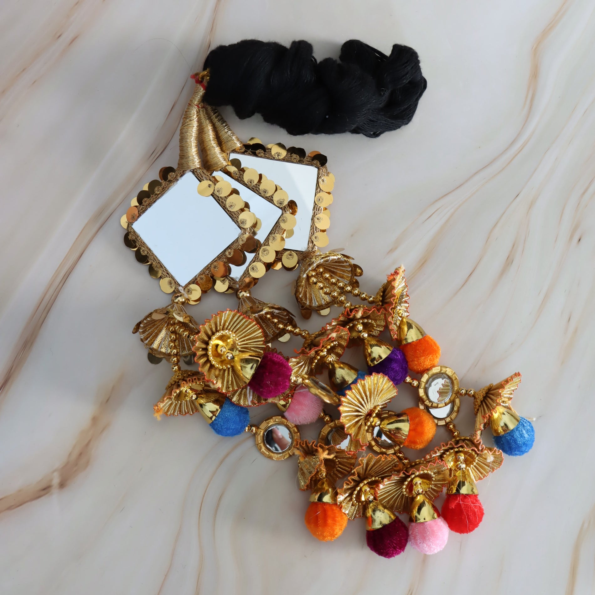 Decorative hair accessory with gold elements and colorful pom-poms on a marble surface