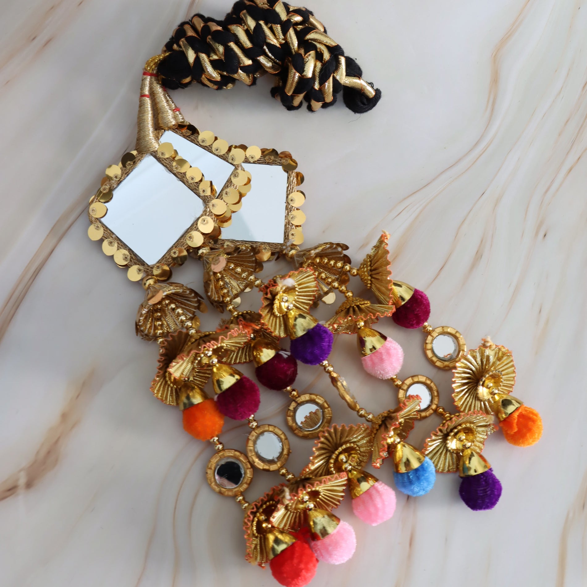 Decorative hair accessory with gold elements and colorful pom-poms on a marble surface