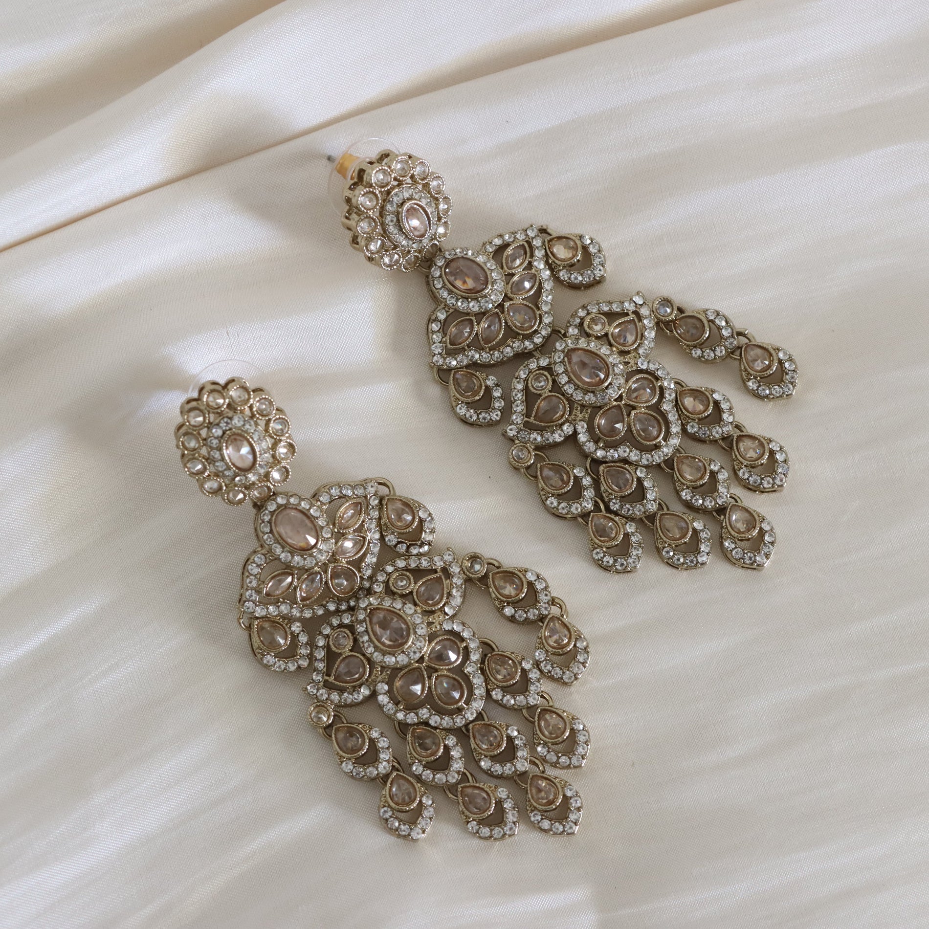 Pair of ornate earrings on a beige fabric background