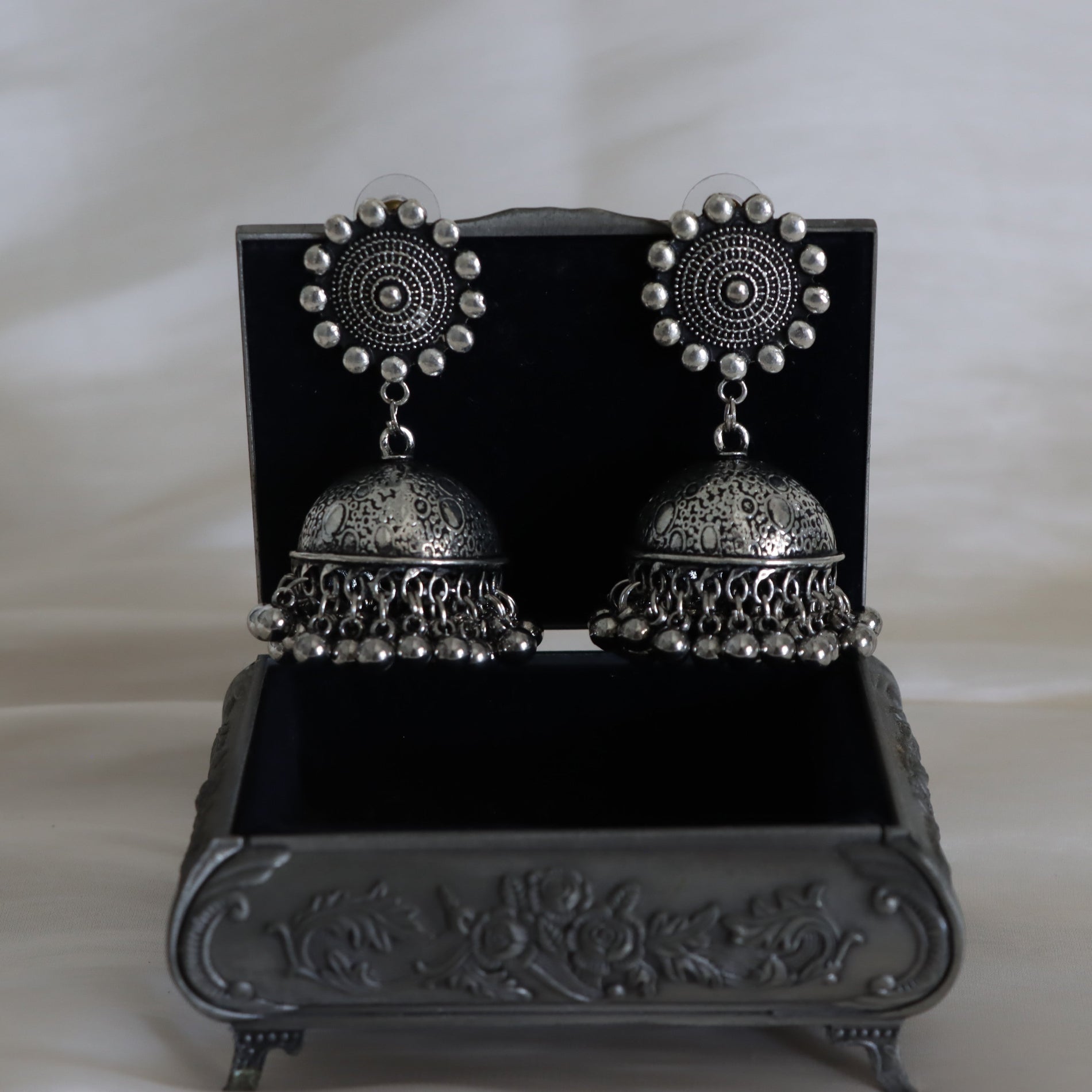 Pair of silver earrings on a decorative black stand with a white background