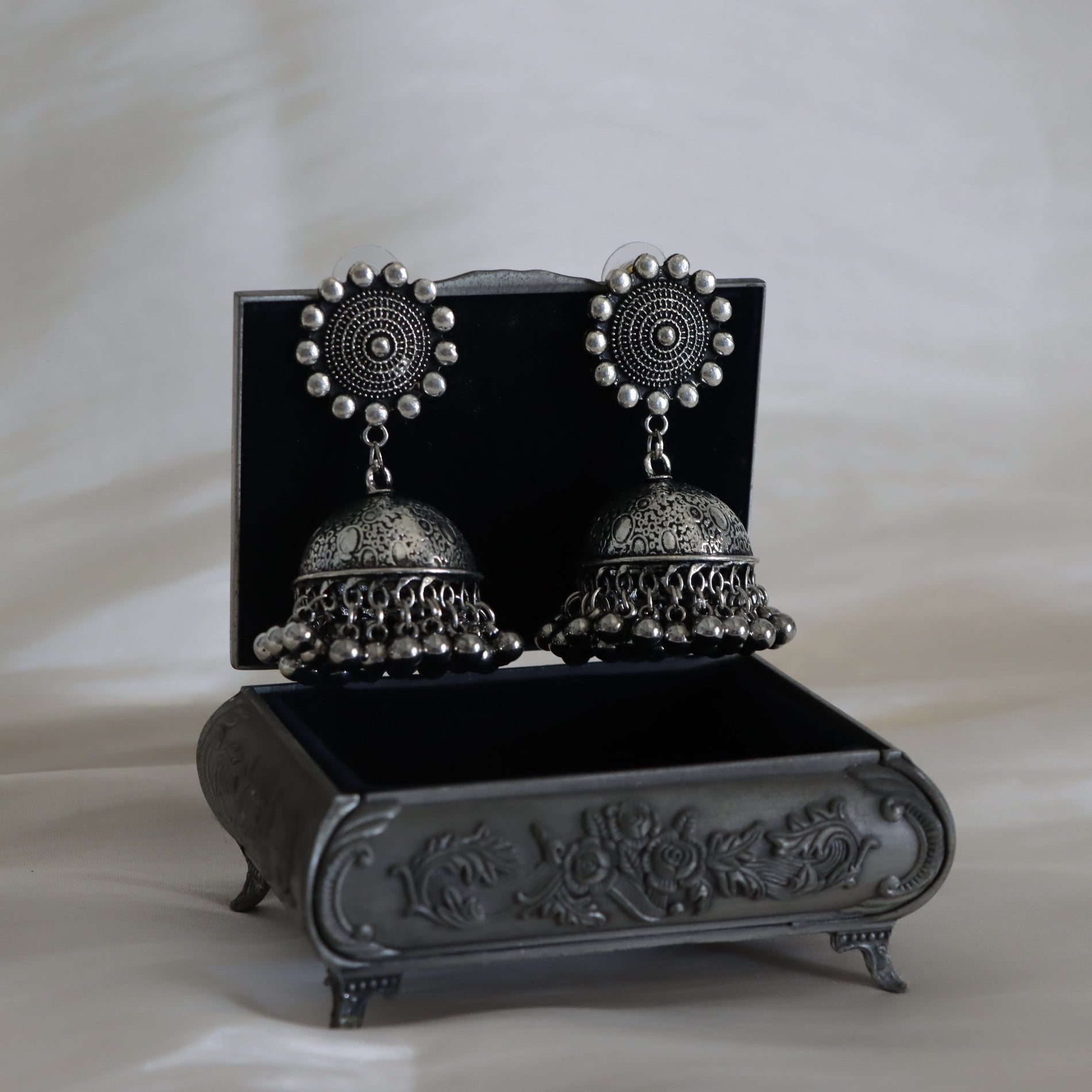 Pair of silver earrings on a decorative black stand with a white background