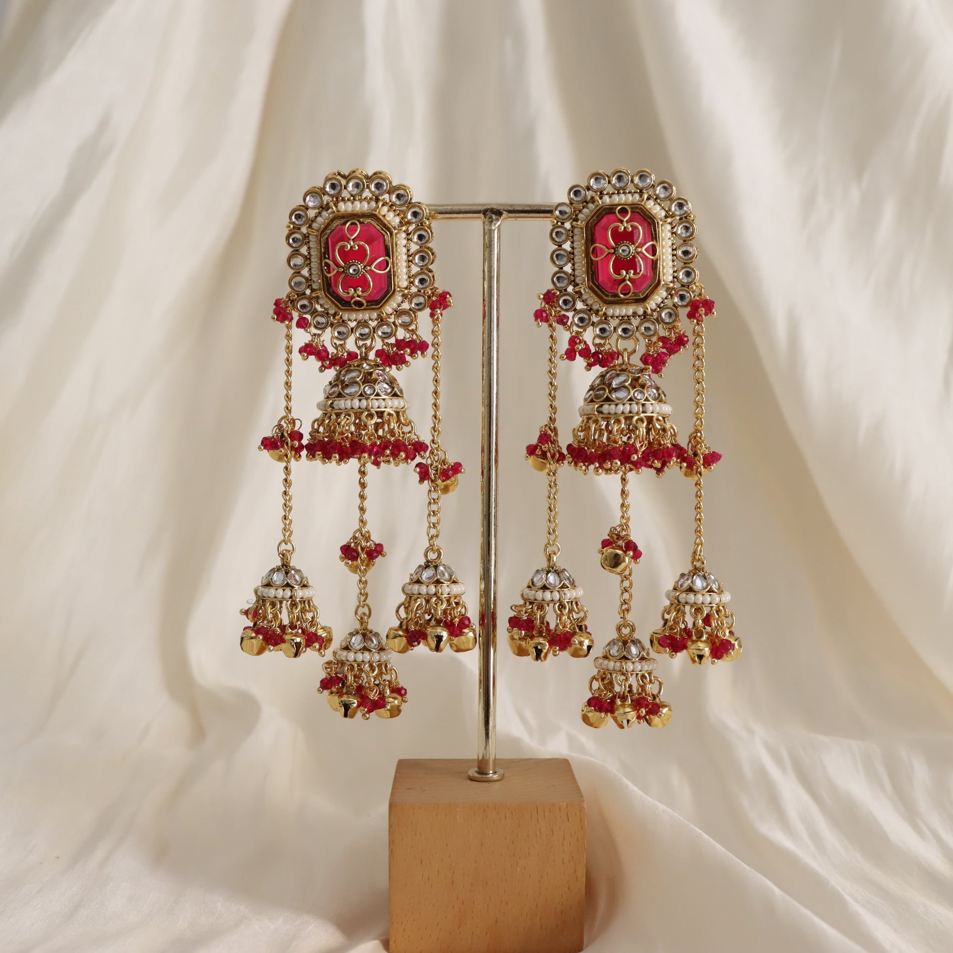 Ornate earrings with red stones on a stand against a white fabric background
