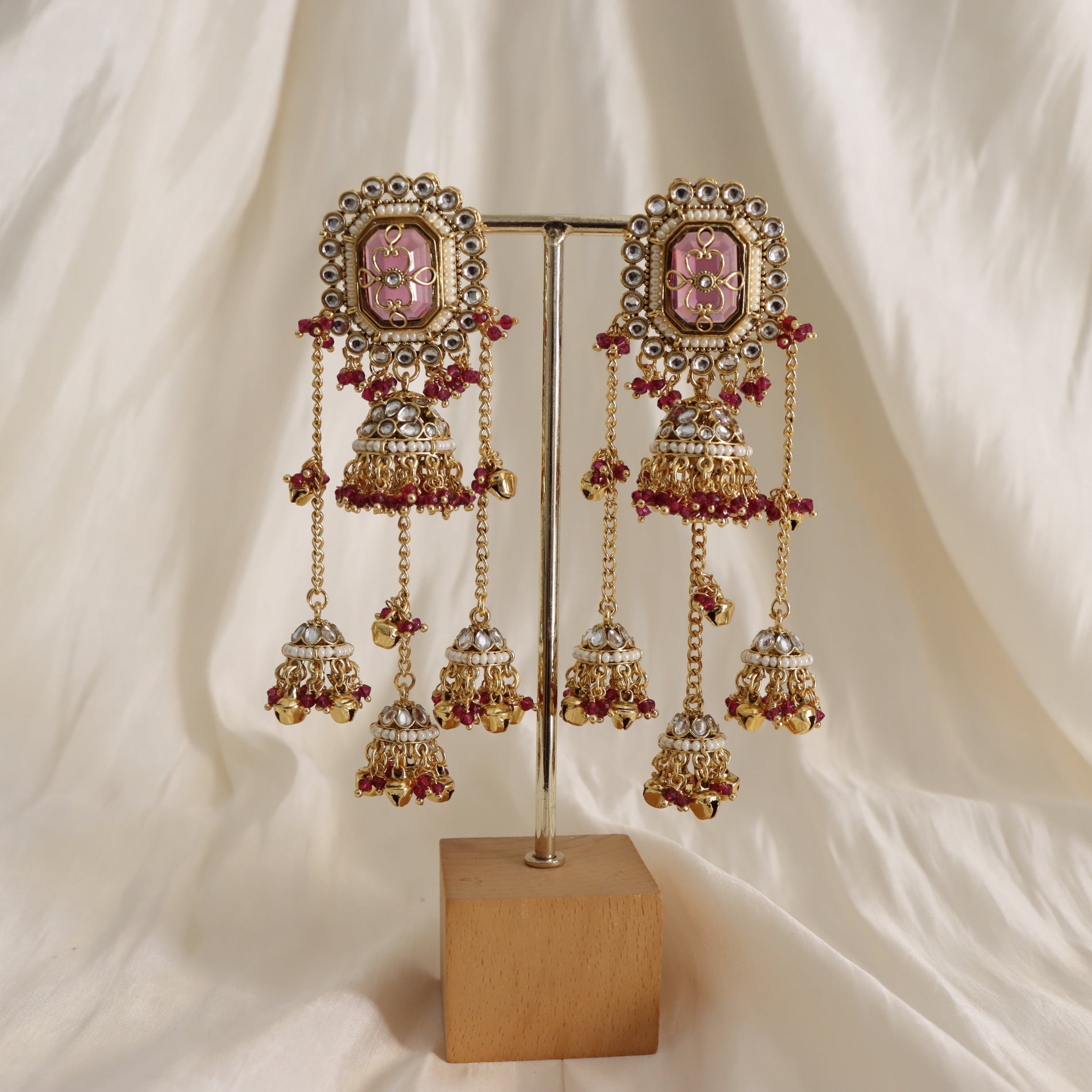 Ornate earrings with pink gemstones on a stand against a white fabric background