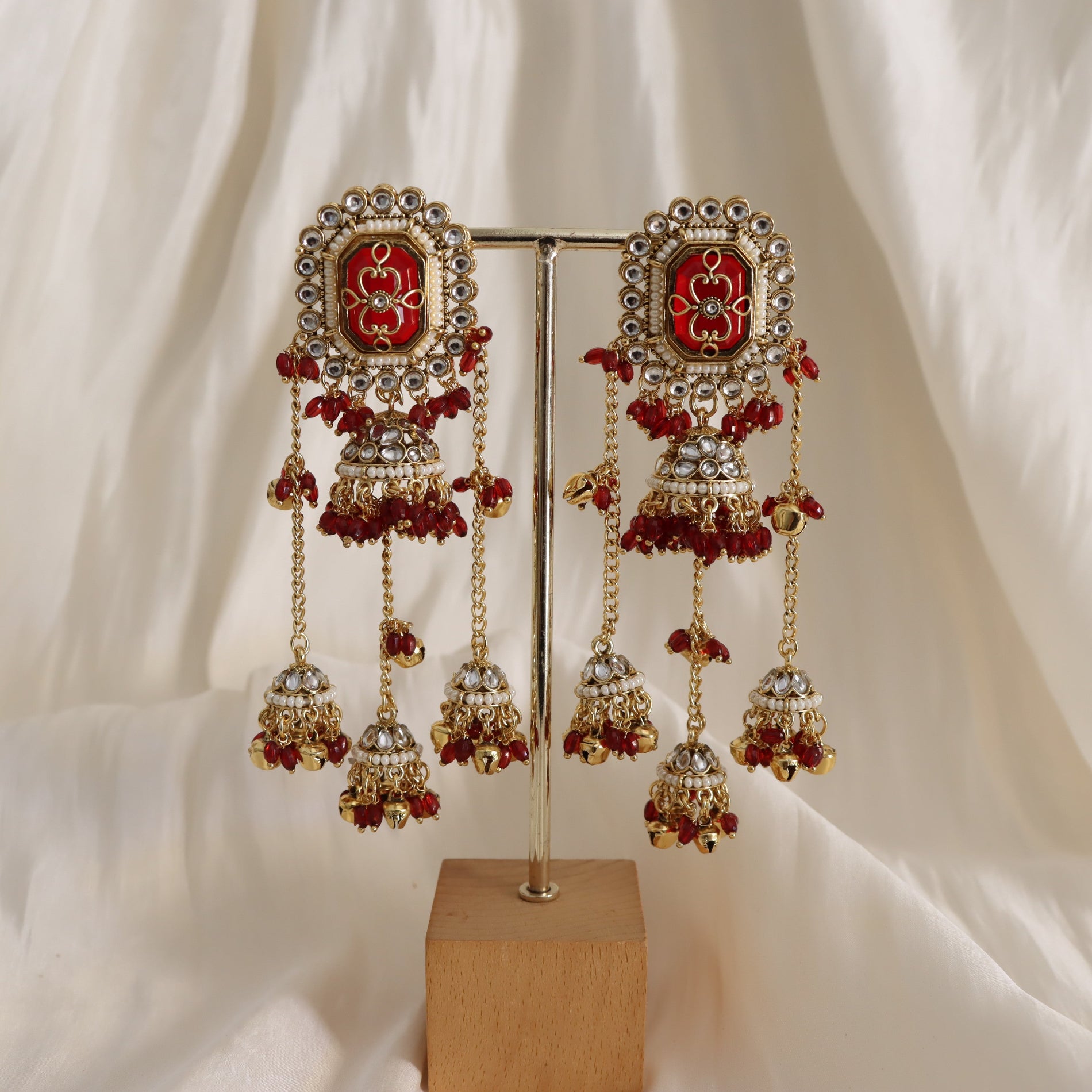 Ornate earrings with red and gold details on a stand against a white fabric background