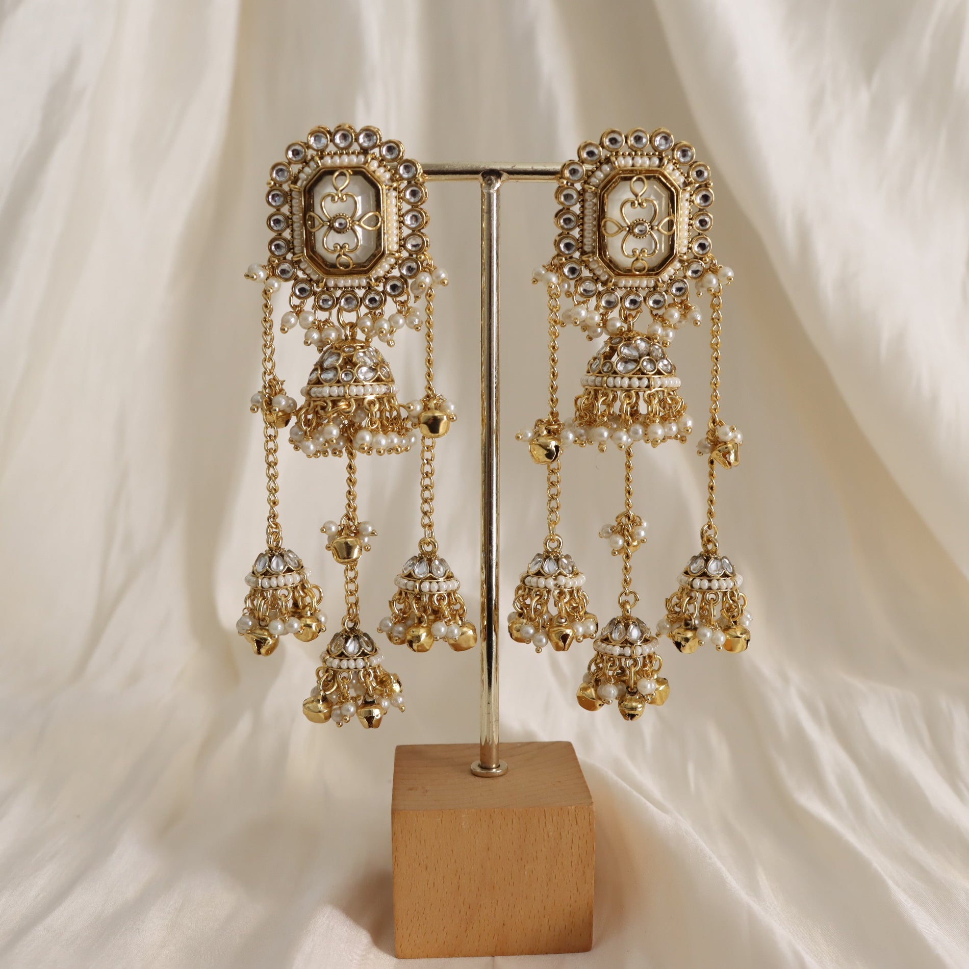 Ornate gold and silver earrings on a stand with a soft white background