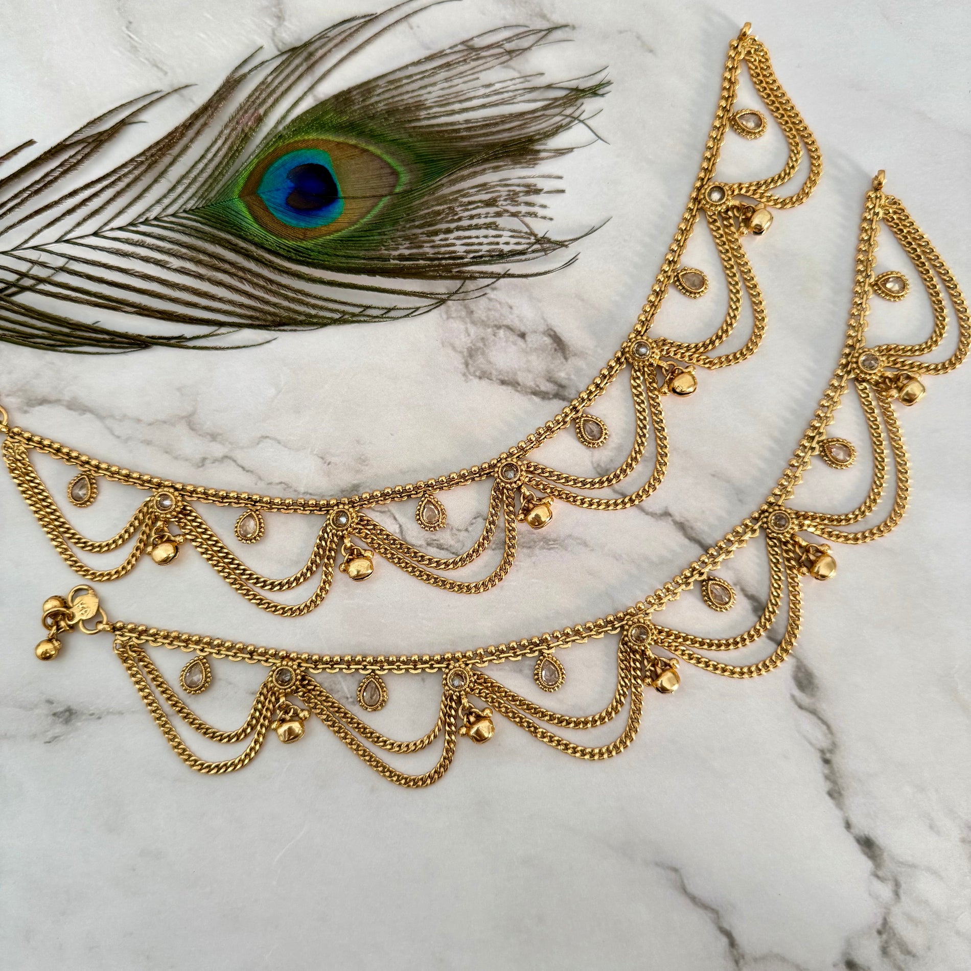 Gold payal on a marble surface with a peacock feather