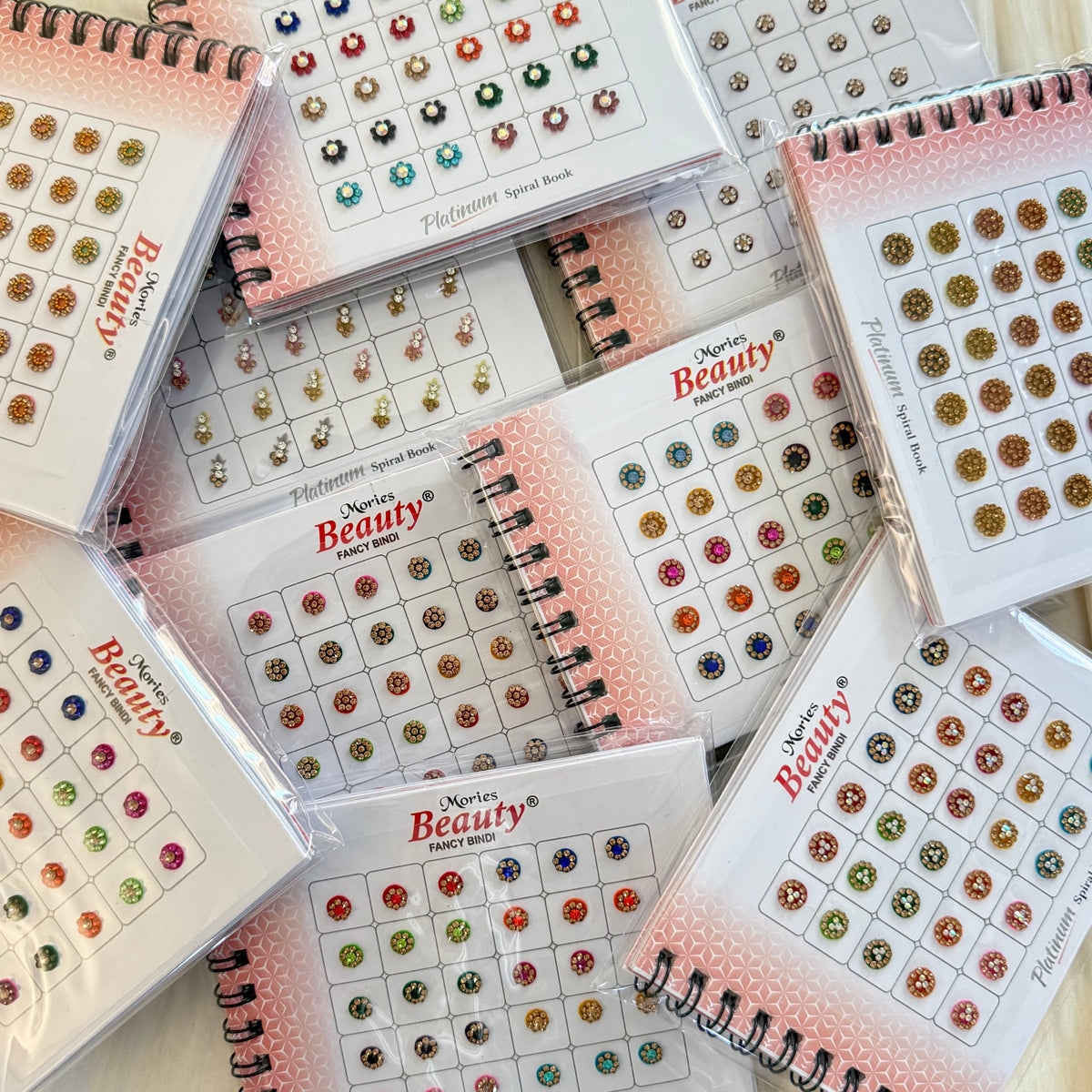 Several spiral-bound beauty reference books titled 'Shimmer Beauty' are arranged in a flat lay, each showing rows of colorful gemstone stud designs on the cover.