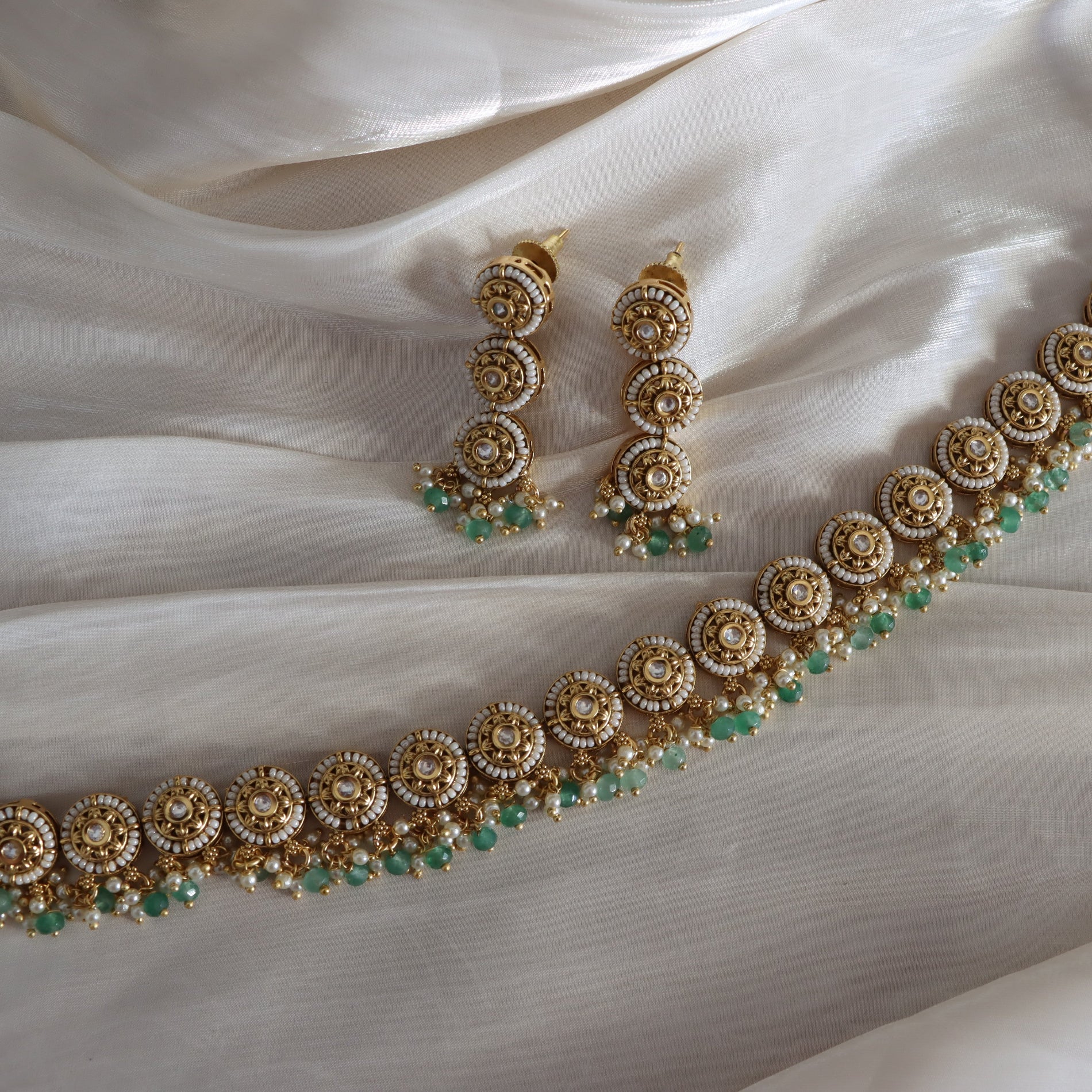 Gold and green jewelry set on a white fabric background
